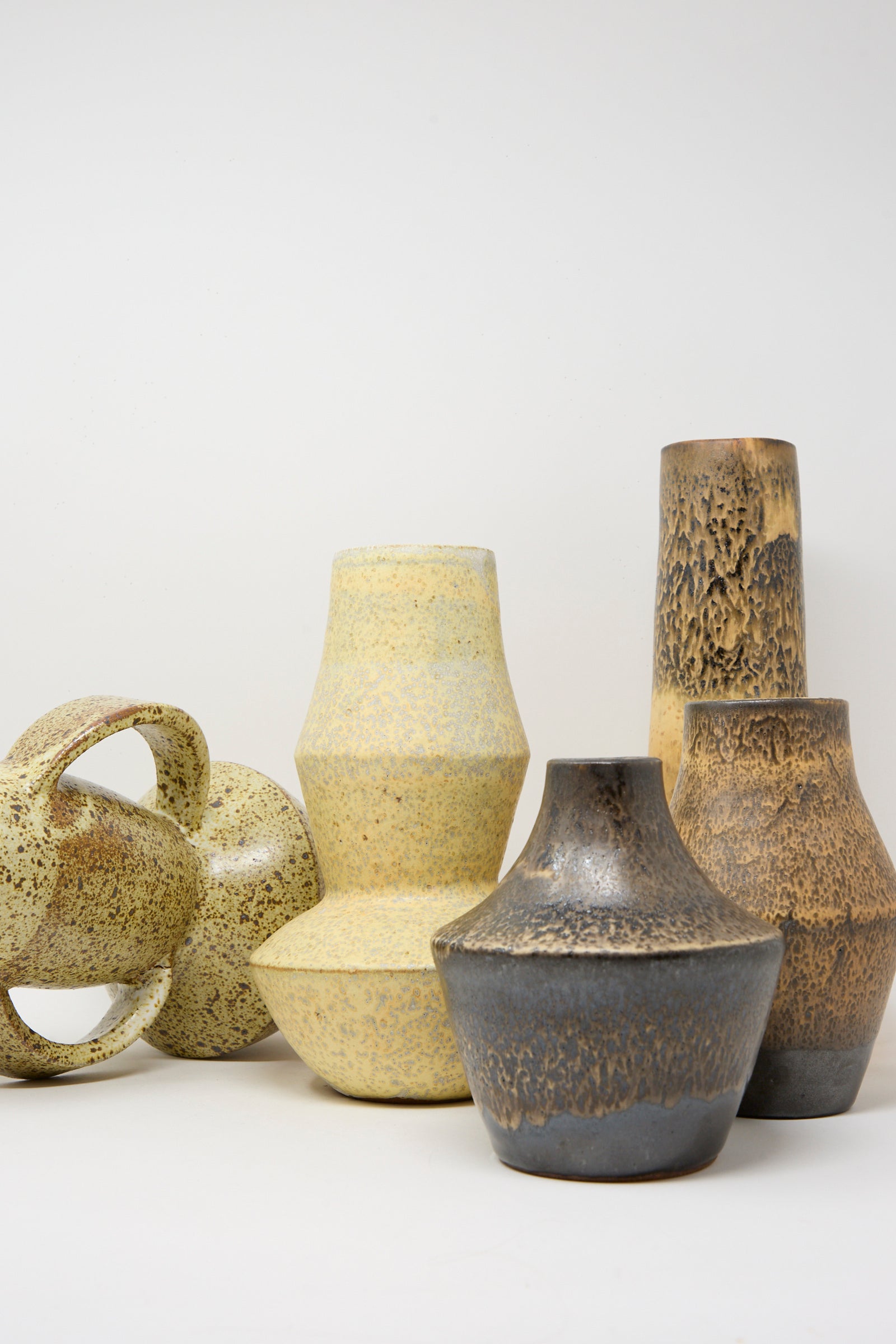 The Rachel Craven Shaped Vase in Eggshell Speckle is featured among six ceramic vases and vessels in neutral tones with varied textures and shapes, all arranged against a plain white background.
