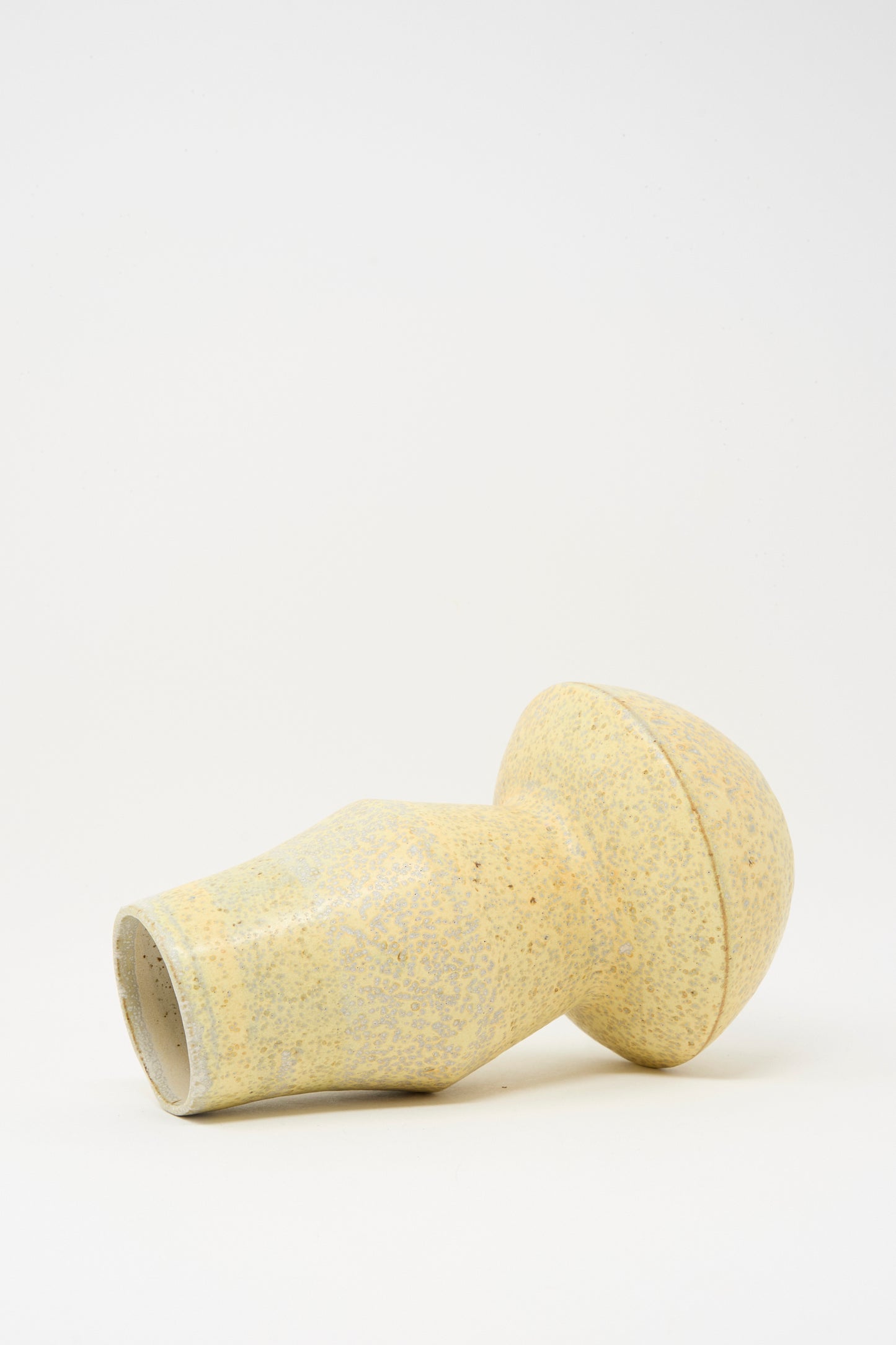 The Shaped Vase in Eggshell Speckle by Rachel Craven, with a cylindrical base and rounded top, is shown on its side against a plain white background.