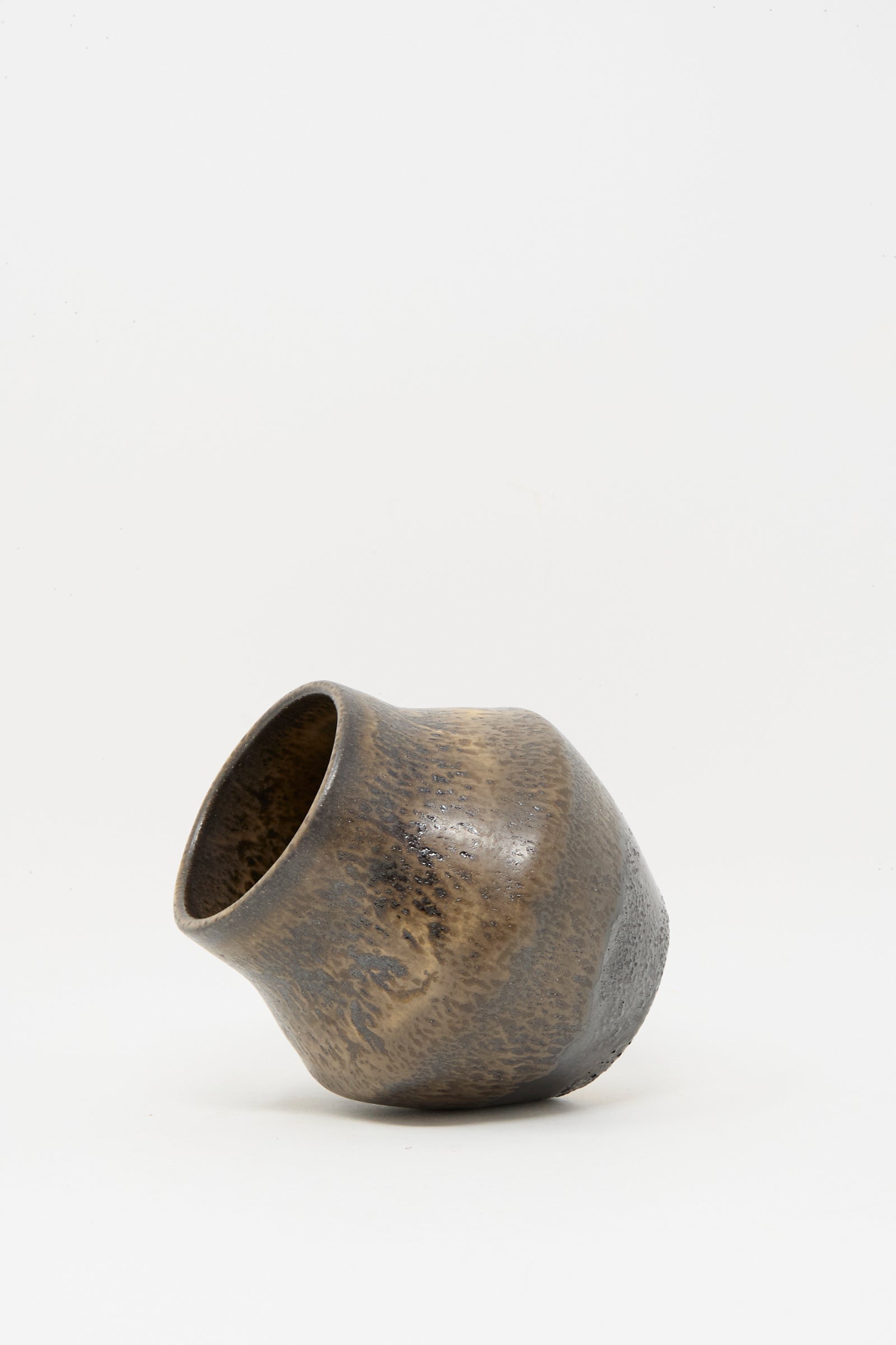 The Small Sap Vase in Black I by Rachel Craven, an unevenly shaped, wheel-thrown clay piece with a brown and gray mineral glaze, rests at an angle on a plain white background.