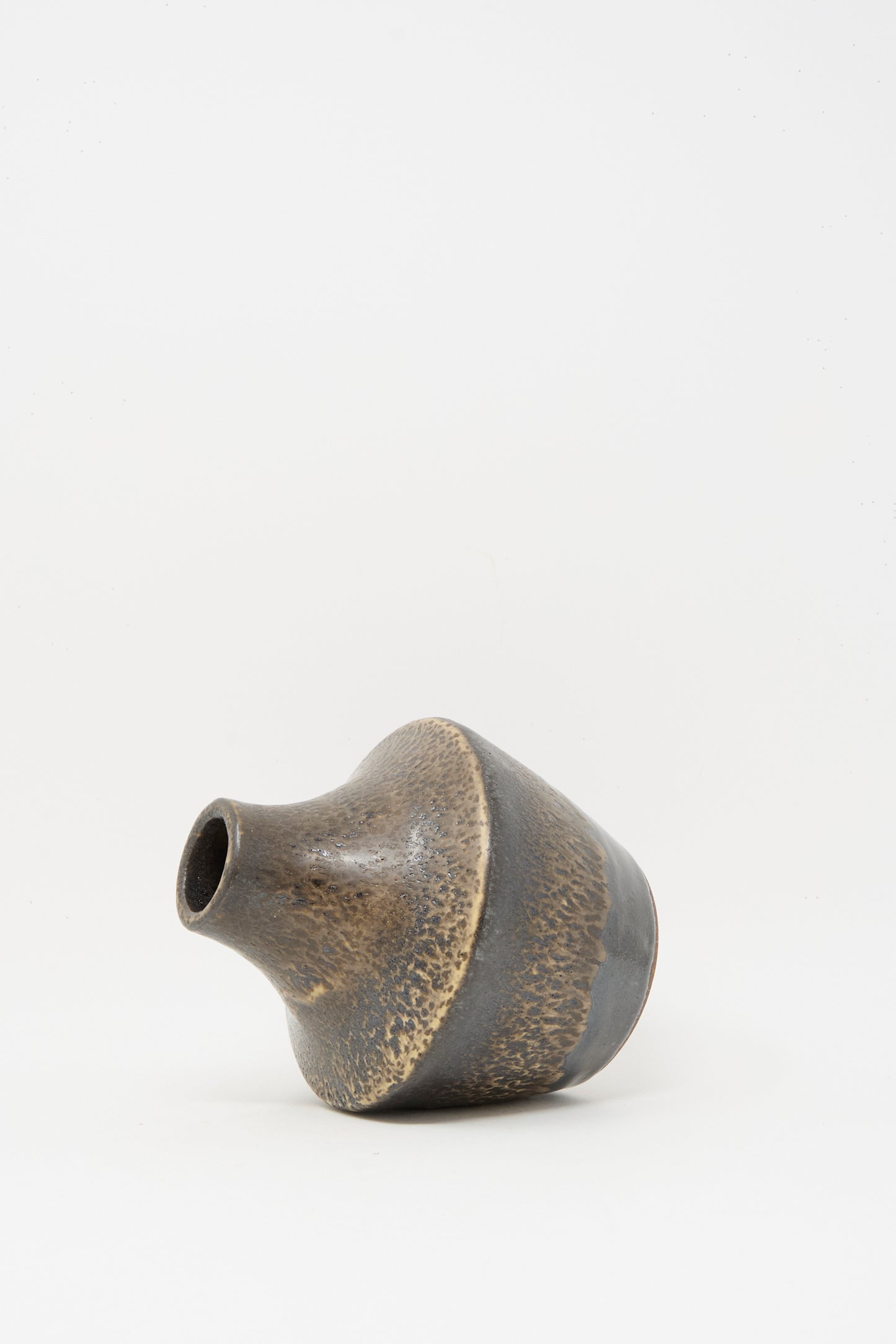 The Small Sap Vase in Black II by Rachel Craven, a wheel-thrown clay vase with a narrow neck and mottled mineral glaze, rests on its side against a plain white background.