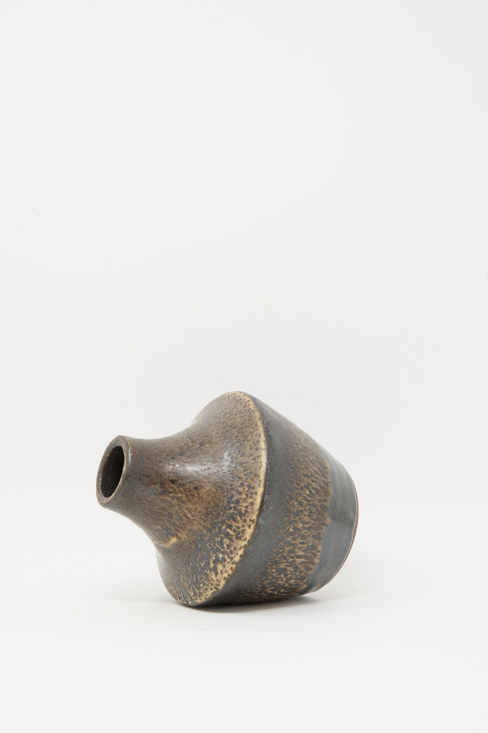 The Small Sap Vase in Black II by Rachel Craven, a wheel-thrown clay vase with a narrow neck and mottled mineral glaze, rests on its side against a plain white background.
