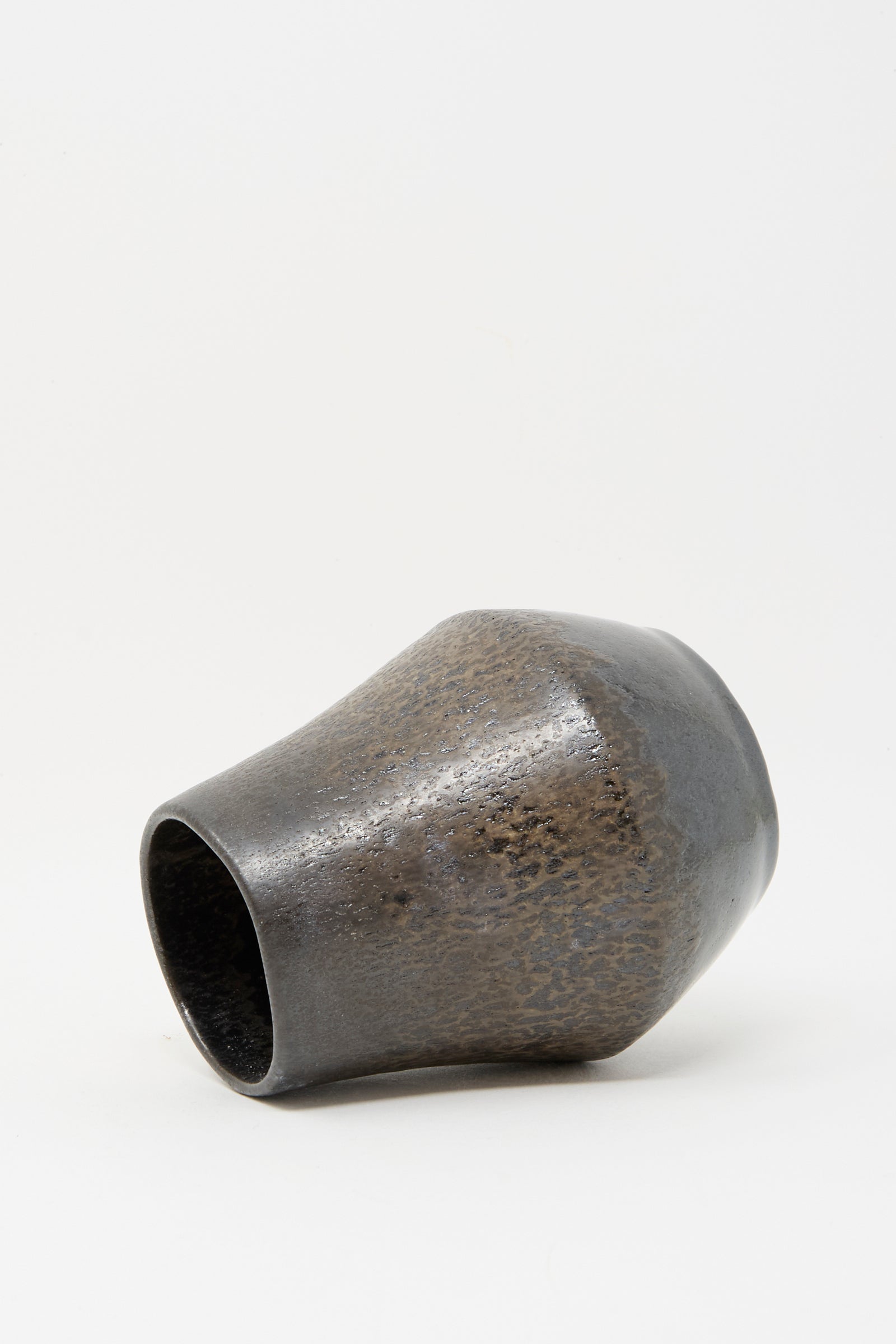 The Small Sap Vase in Black III by Rachel Craven, featuring a textured handmade design and wide opening with a metallic finish, rests on its side against a plain white background.