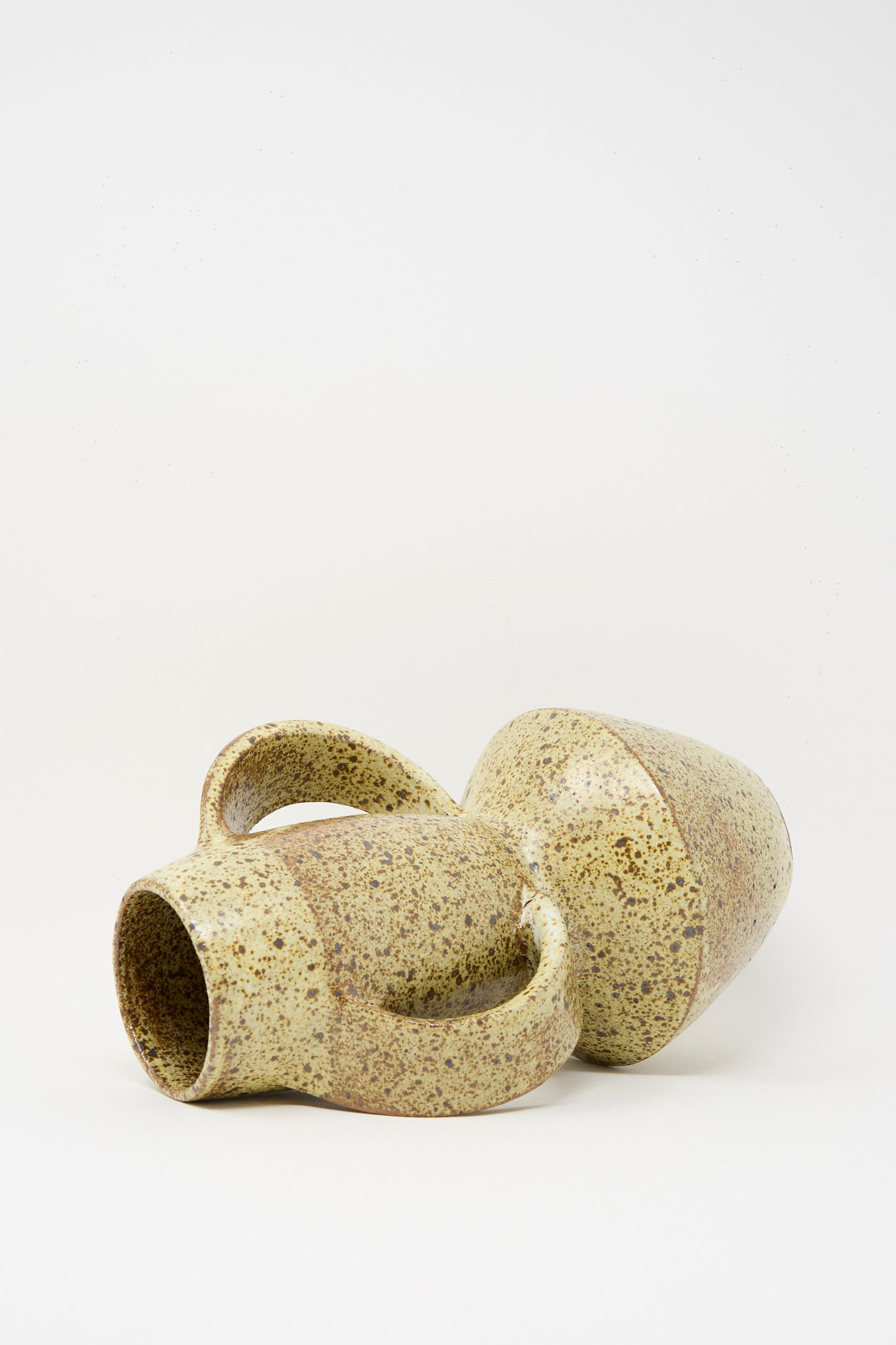 The Tall Shaped Handled Vase in Eggshell Speckle by Rachel Craven rests on its side against a plain white background, its mineral glaze and speckled finish catching the light.