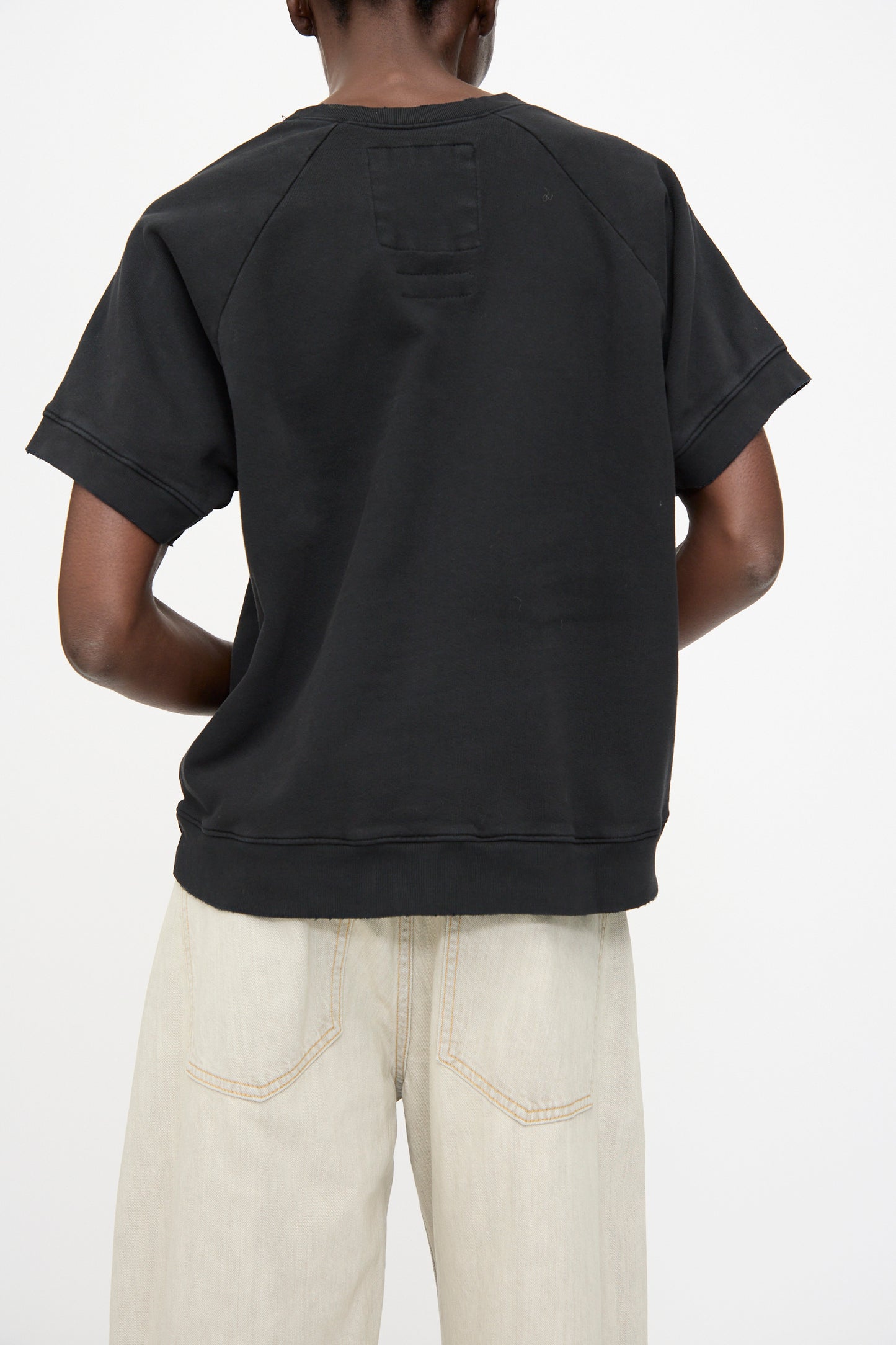 Model shown from the back wearing the Rachel Comey Billi Sweatshirt in Charcoal, a black 100% cotton crewneck short sleeve top, paired with light-colored jeans against a plain white background.