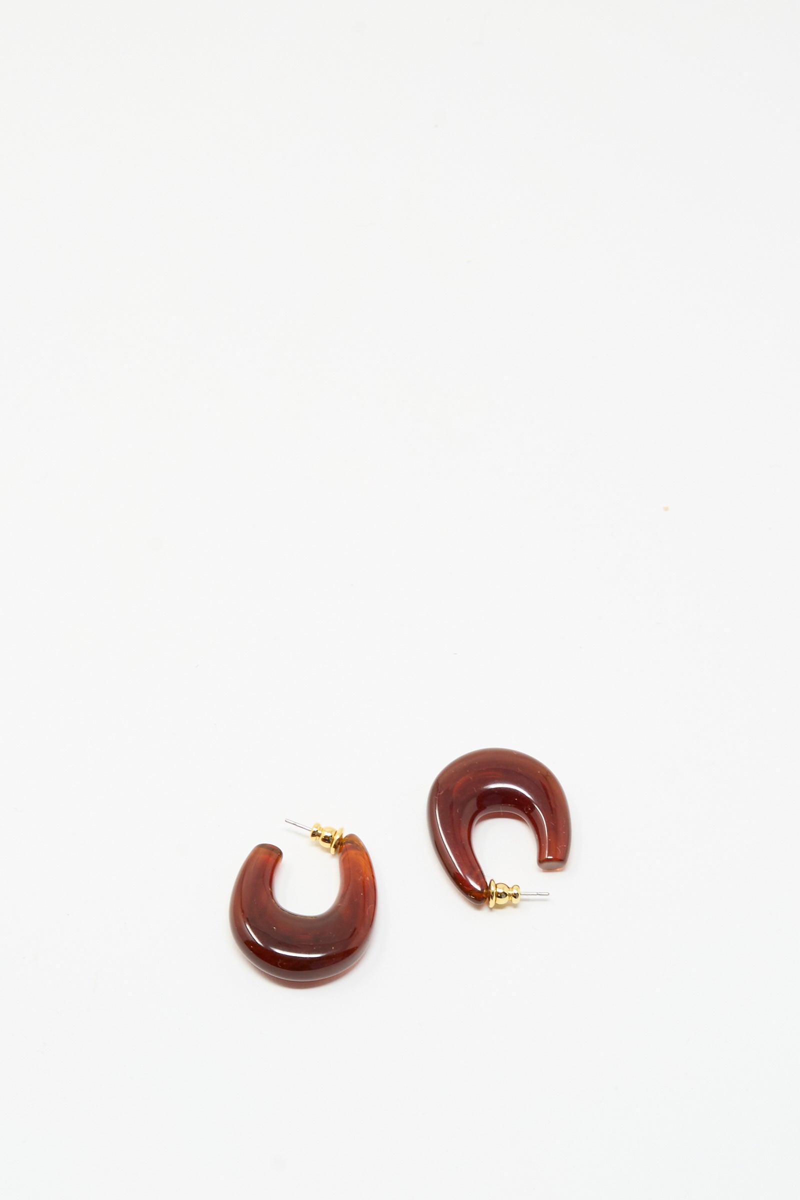 The Rachel Comey Isle Earrings in Dark Tortoise feature brown, semi-circular chunky acrylic hoops with gold posts, shown against a plain white background.