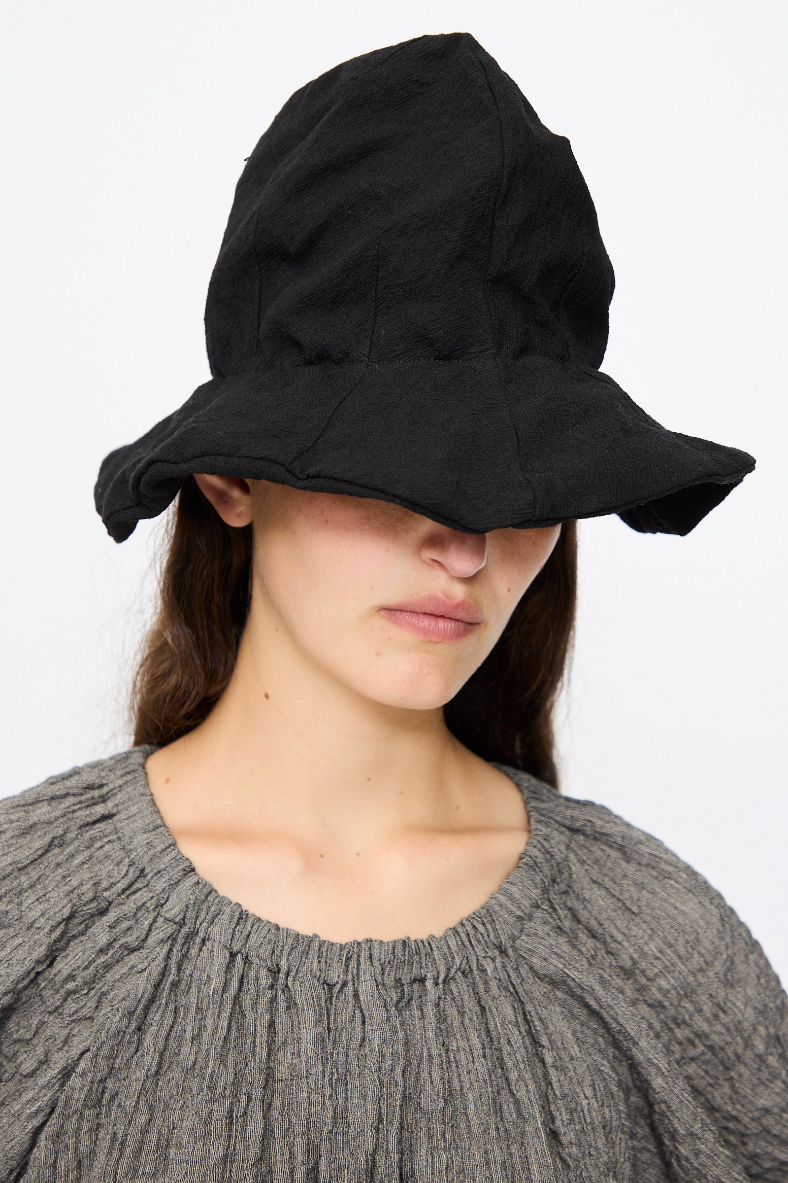 A person wears the Reinhard Plank Cotton Ces Hat in Black with a textured grey premium cotton top, partially hiding their face, set against a plain white background.
