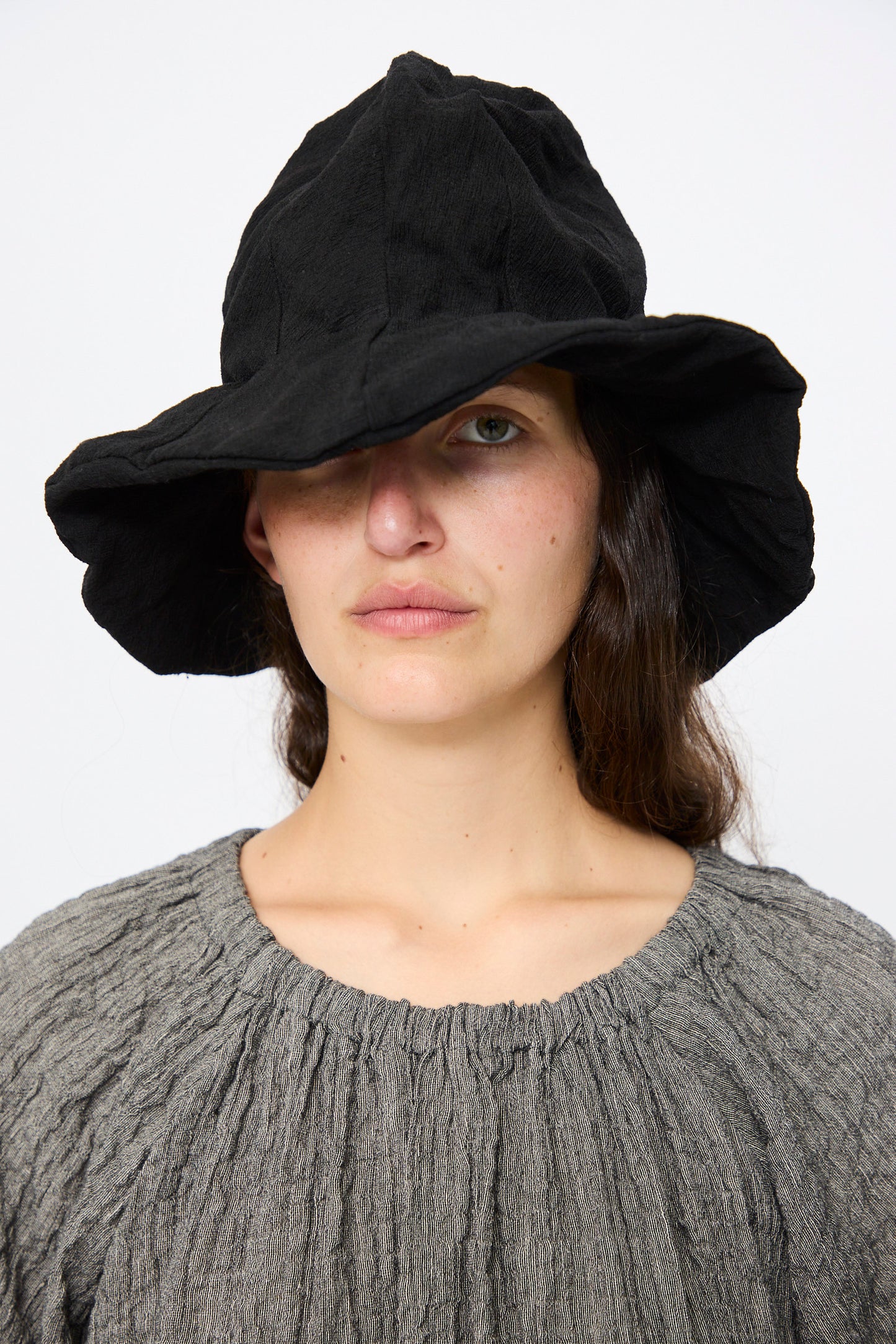 A person wearing the Reinhard Plank Cotton Ces Hat in Black and a gray premium cotton top looks directly at the camera with a neutral expression.