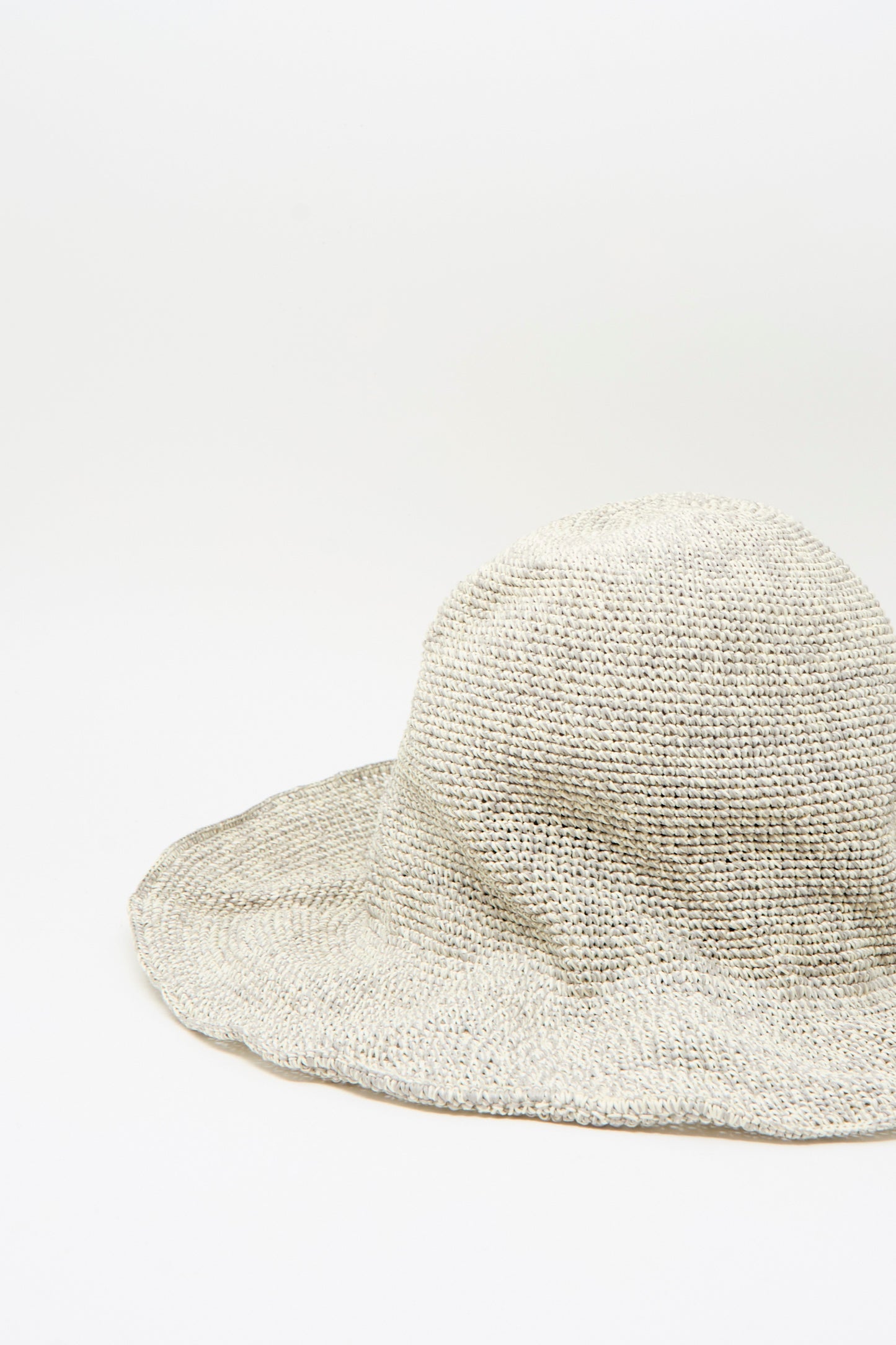 The Isle New Paper Hat in White, Sand by Reinhard Plank, a light-colored wide-brimmed crocheted paper hat, rests on a plain white surface with a simple background.