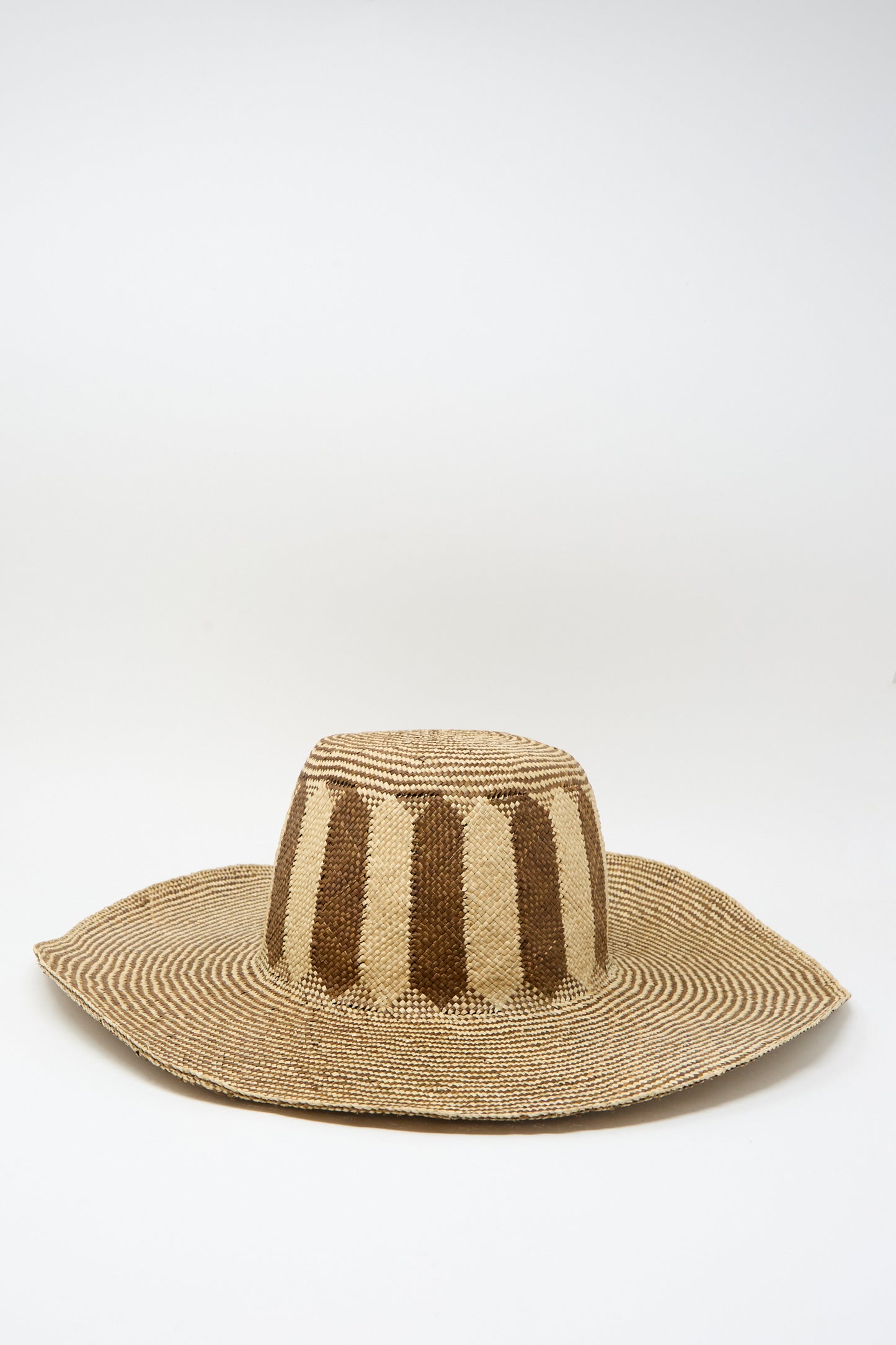 The Reinhard Plank Straw Beghe Lai Hat in Natural Stripes is a wide-brimmed Italian-made straw hat with alternating vertical light and dark brown stripes on the crown and a circular striped pattern on the brim.
