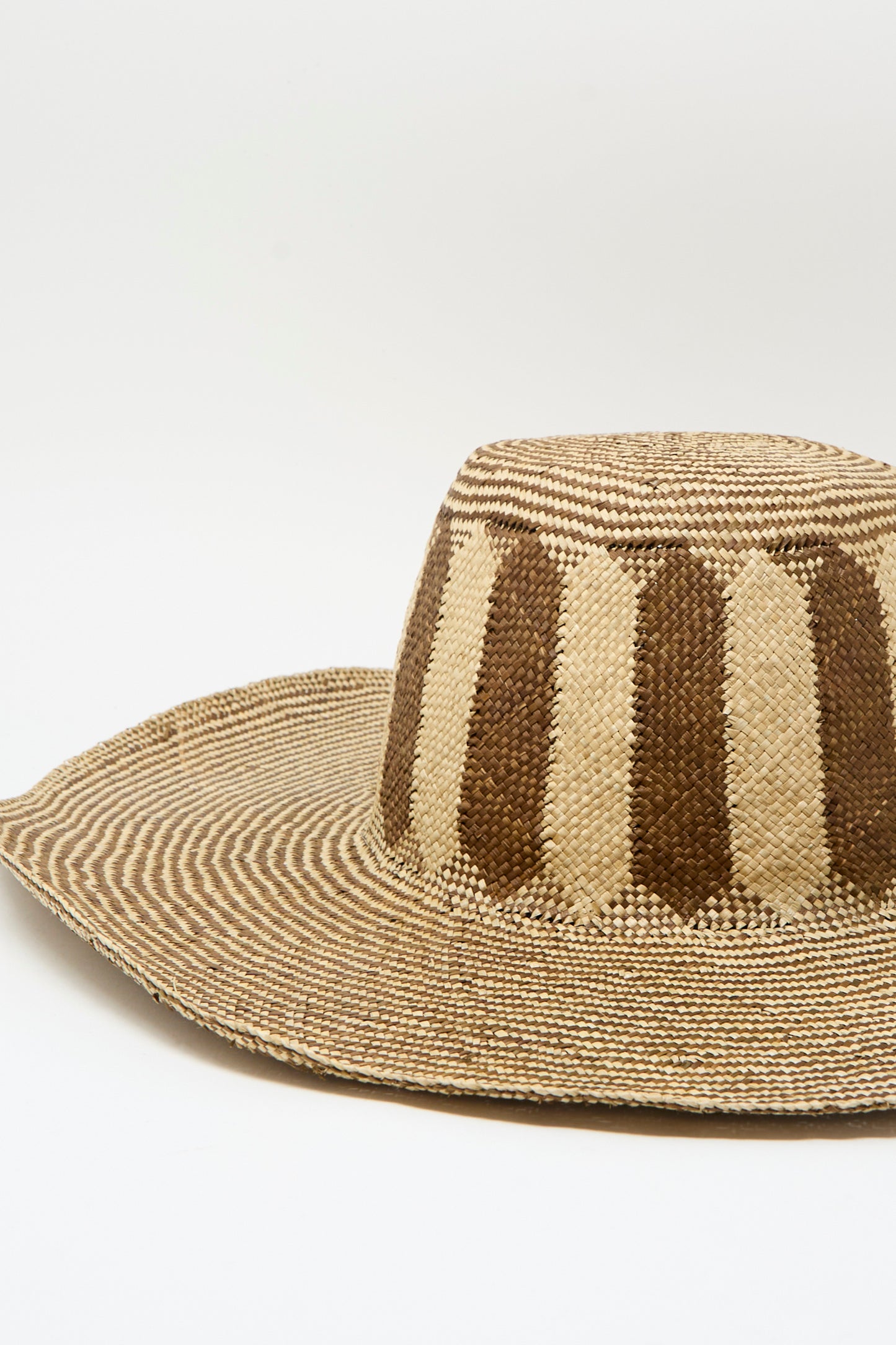 The Reinhard Plank Straw Beghe Lai Hat in Natural Stripes, made in Italy, features a wide brim and alternating dark and light vertical stripes on the crown, shown against a plain white background.