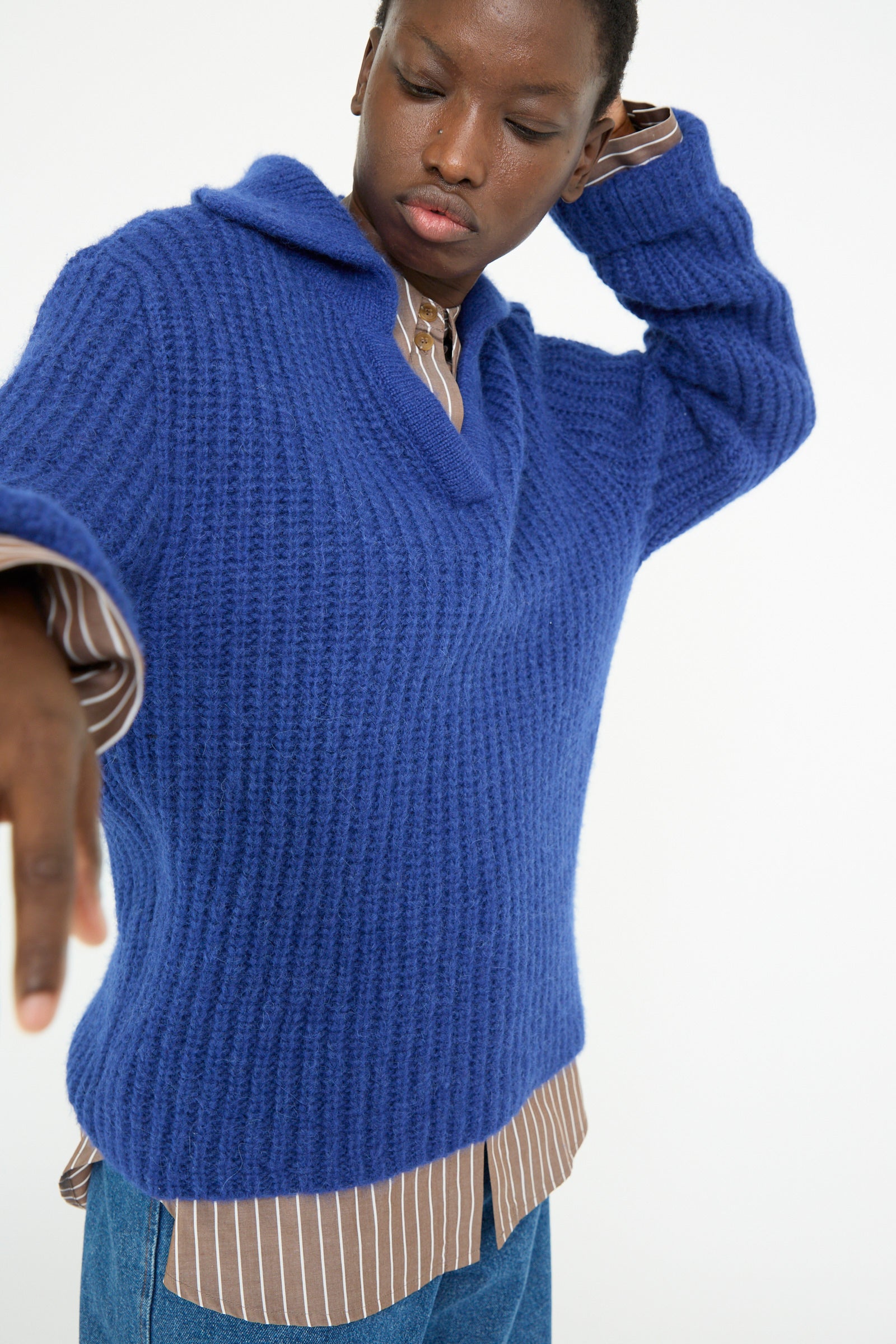 A person poses against a white background wearing the Rejina Pyo Chunky Alpaca Alison Sweater in electric blue over a brown striped shirt.