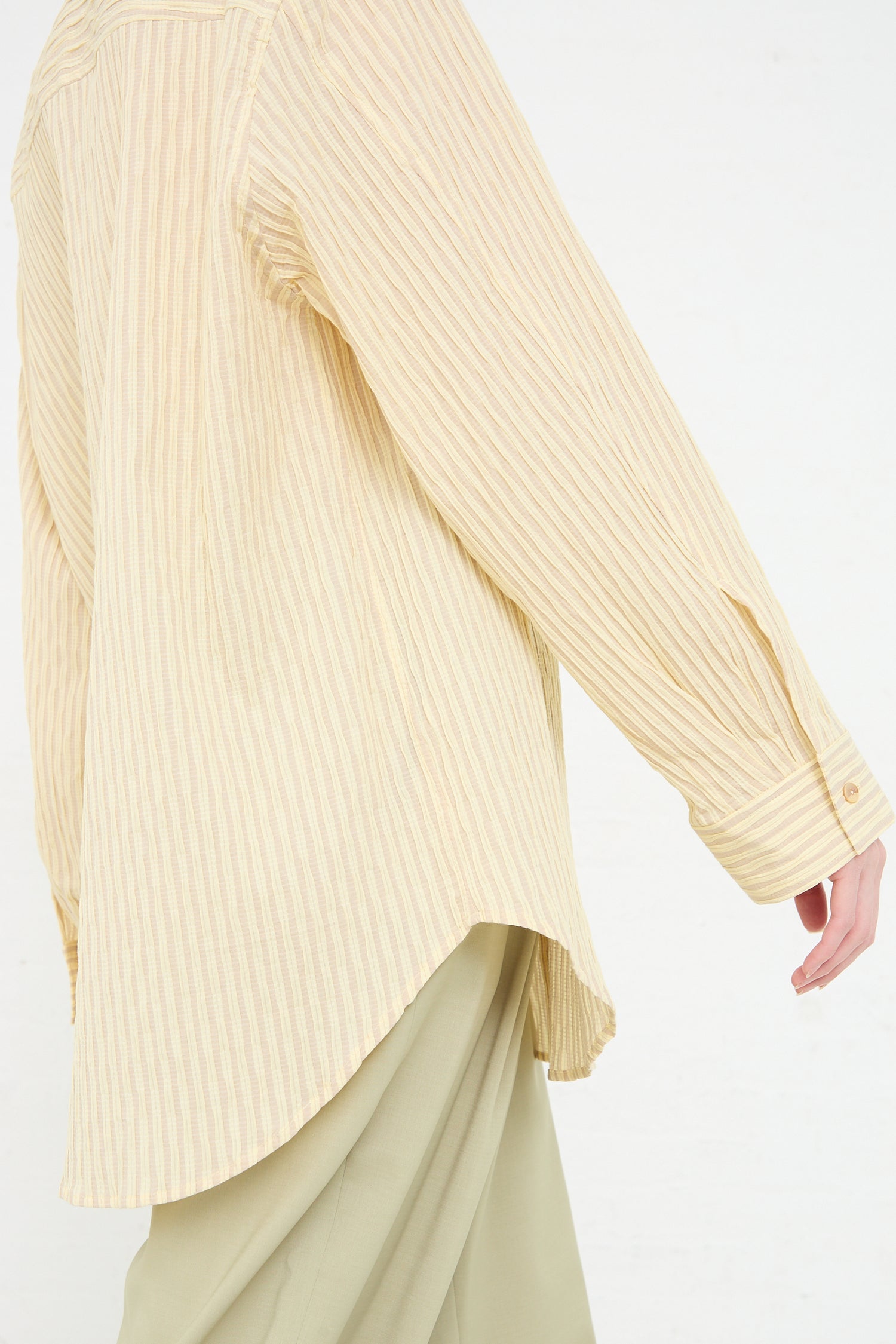 Close-up of a person wearing a Rejina Pyo Organic Cotton Seersucker Caprice Shirt in Stripe Yellow and green trousers, focusing on the fabric and style details.