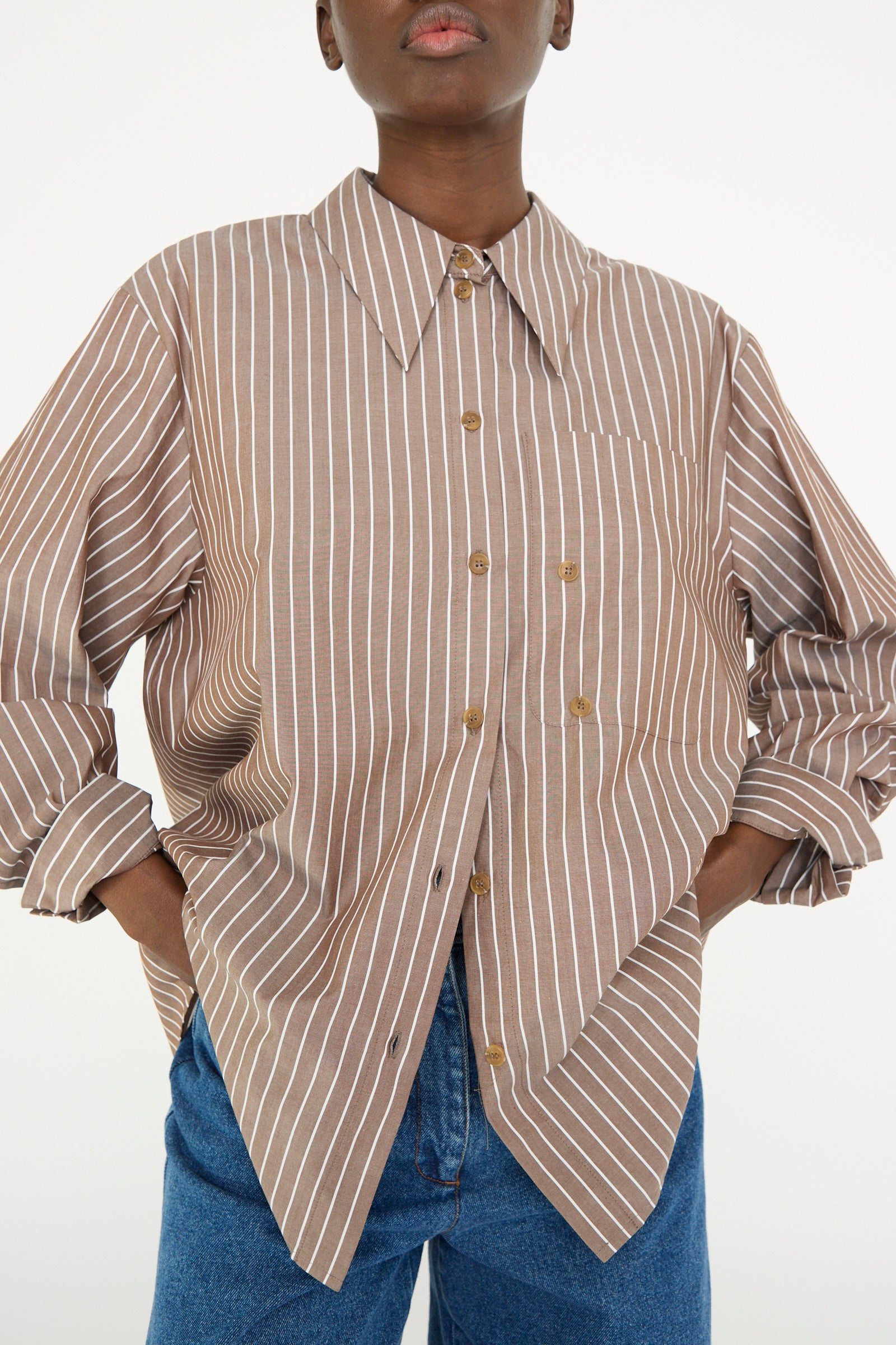 Person wearing Rejina Pyo's Cotton Stripe Ellis Shirt in Brown with blue jeans, hands in pockets.