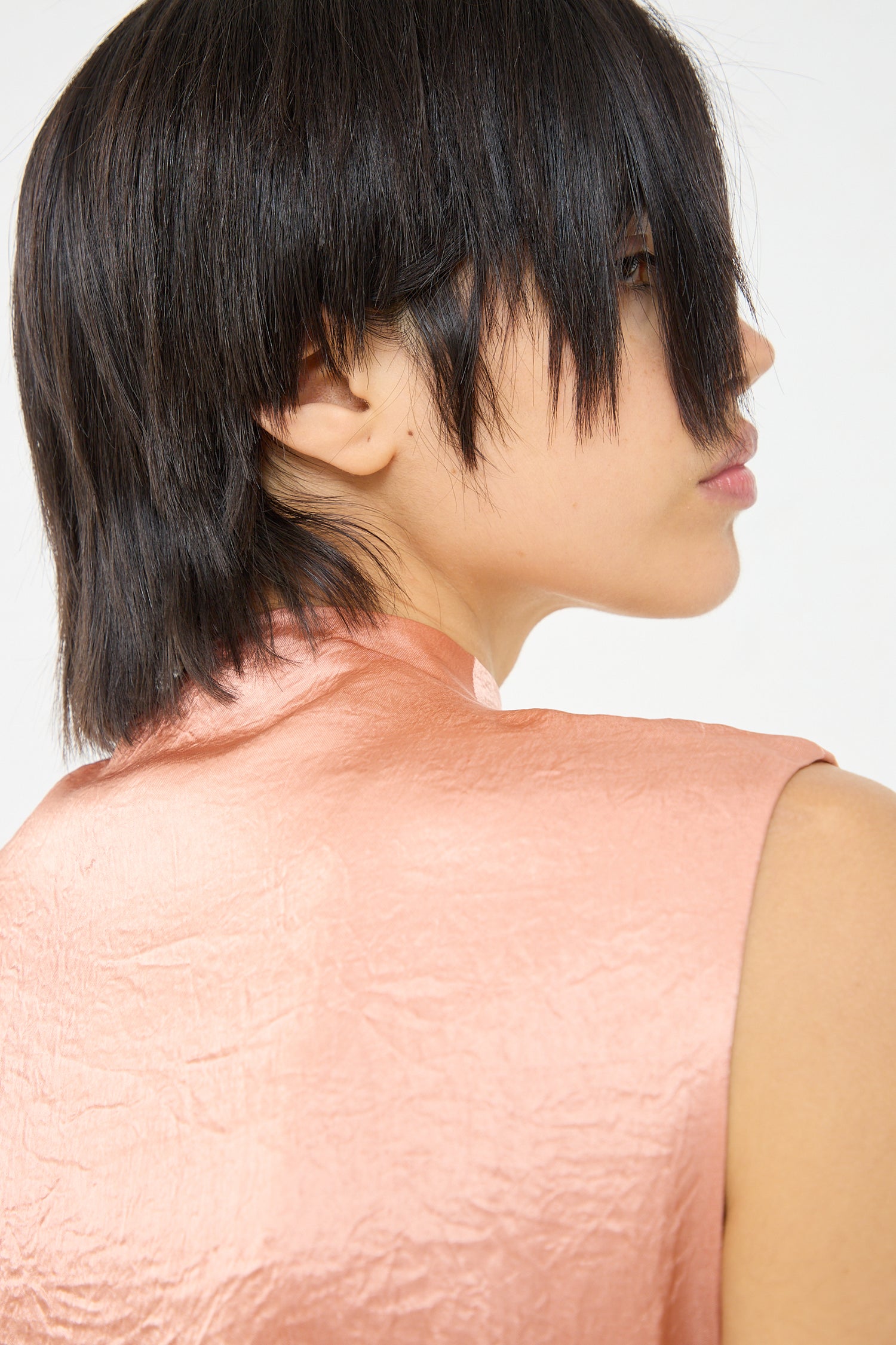 The back view of a woman wearing a Rejina Pyo Delilah Dress in Pink acetate satin top. Up close view.