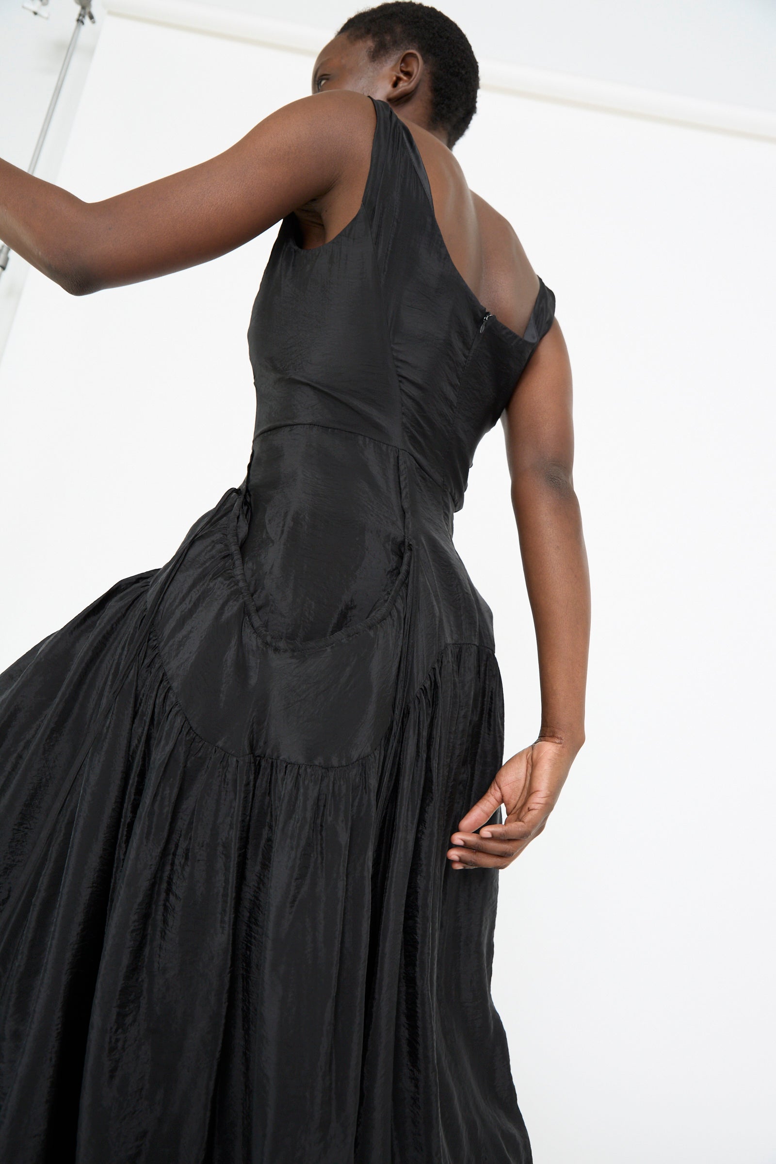 Someone wears the Erica Dress in Black by Rejina Pyo, featuring a flowing, sleeveless midi design with a corseted bodice, expertly crafted from a luxurious viscose blend.