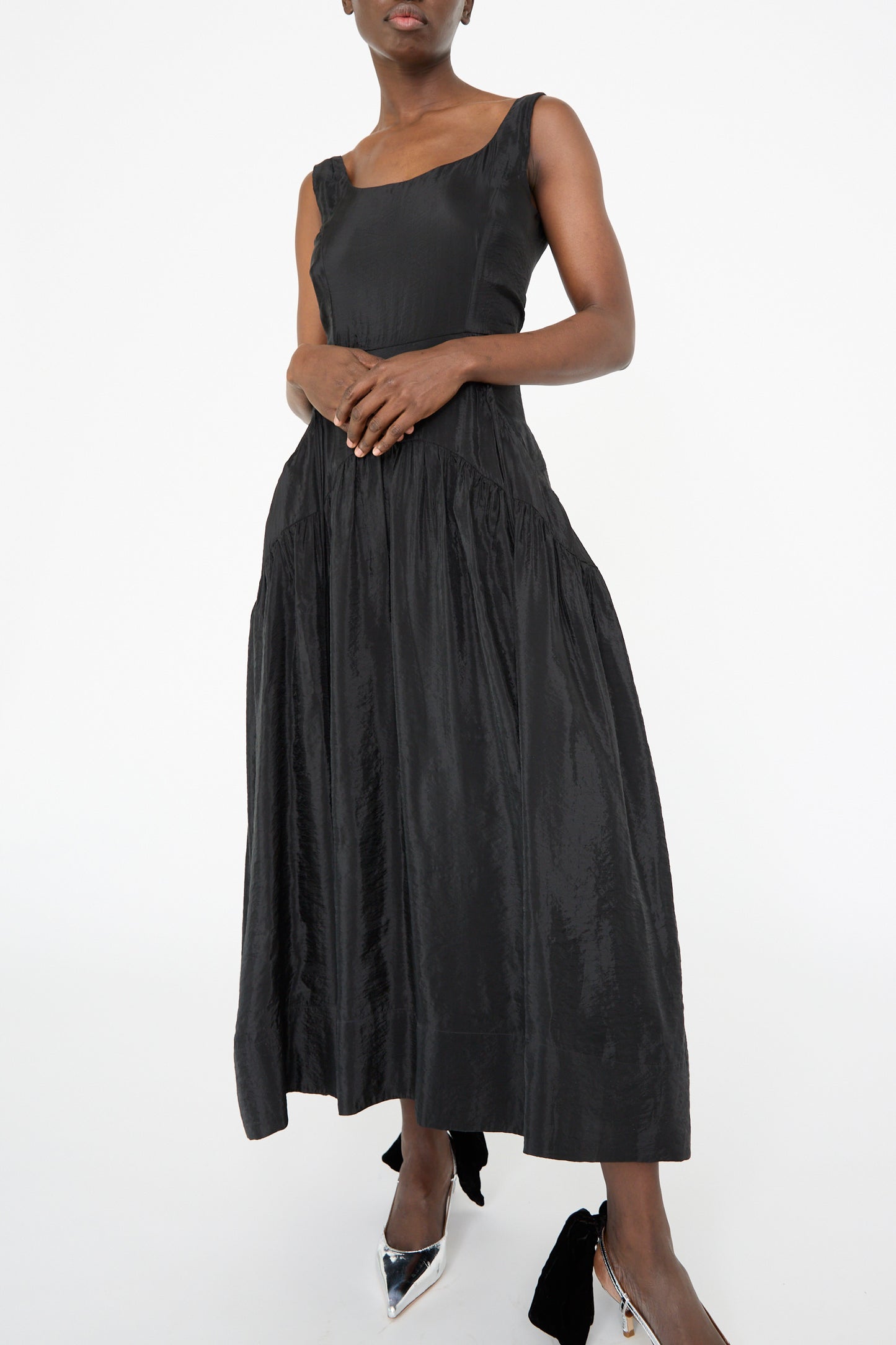 A person poses against a plain background wearing the Rejina Pyo Erica Dress in Black: a sleeveless midi dress featuring a pleated skirt and corseted bodice.