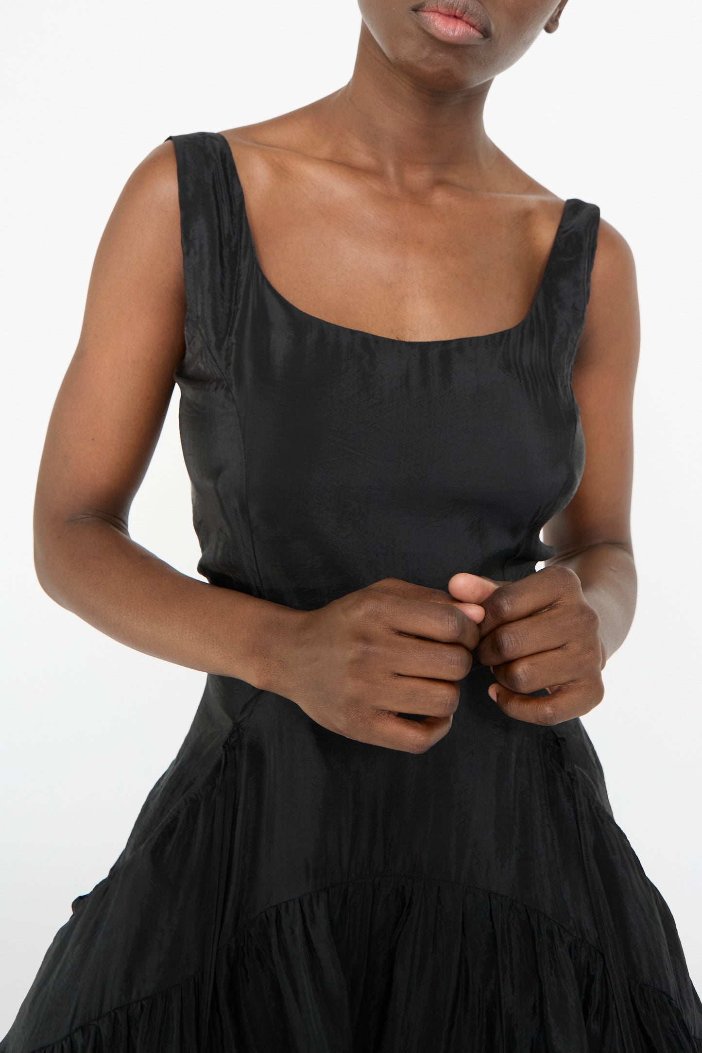 A person elegantly stands against a plain background wearing the Erica Dress in Black by Rejina Pyo, featuring a scoop neckline and corseted bodice.