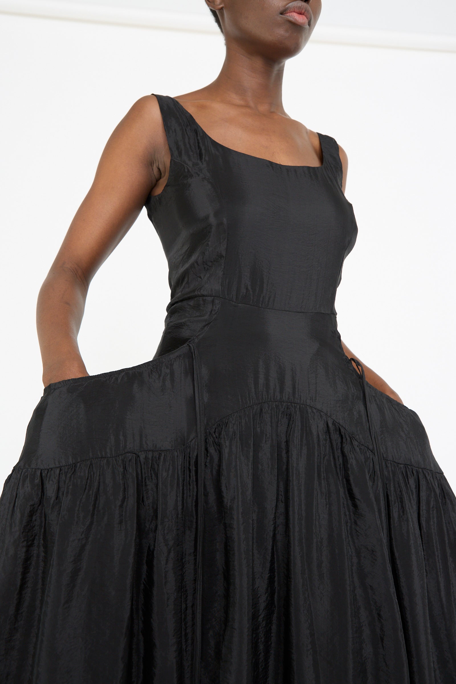 A model showcases the Erica Dress in Black by Rejina Pyo, featuring a sleeveless midi design in a viscose blend with a corseted bodice that enhances the fitted silhouette and voluminous skirt, set against a plain white background.