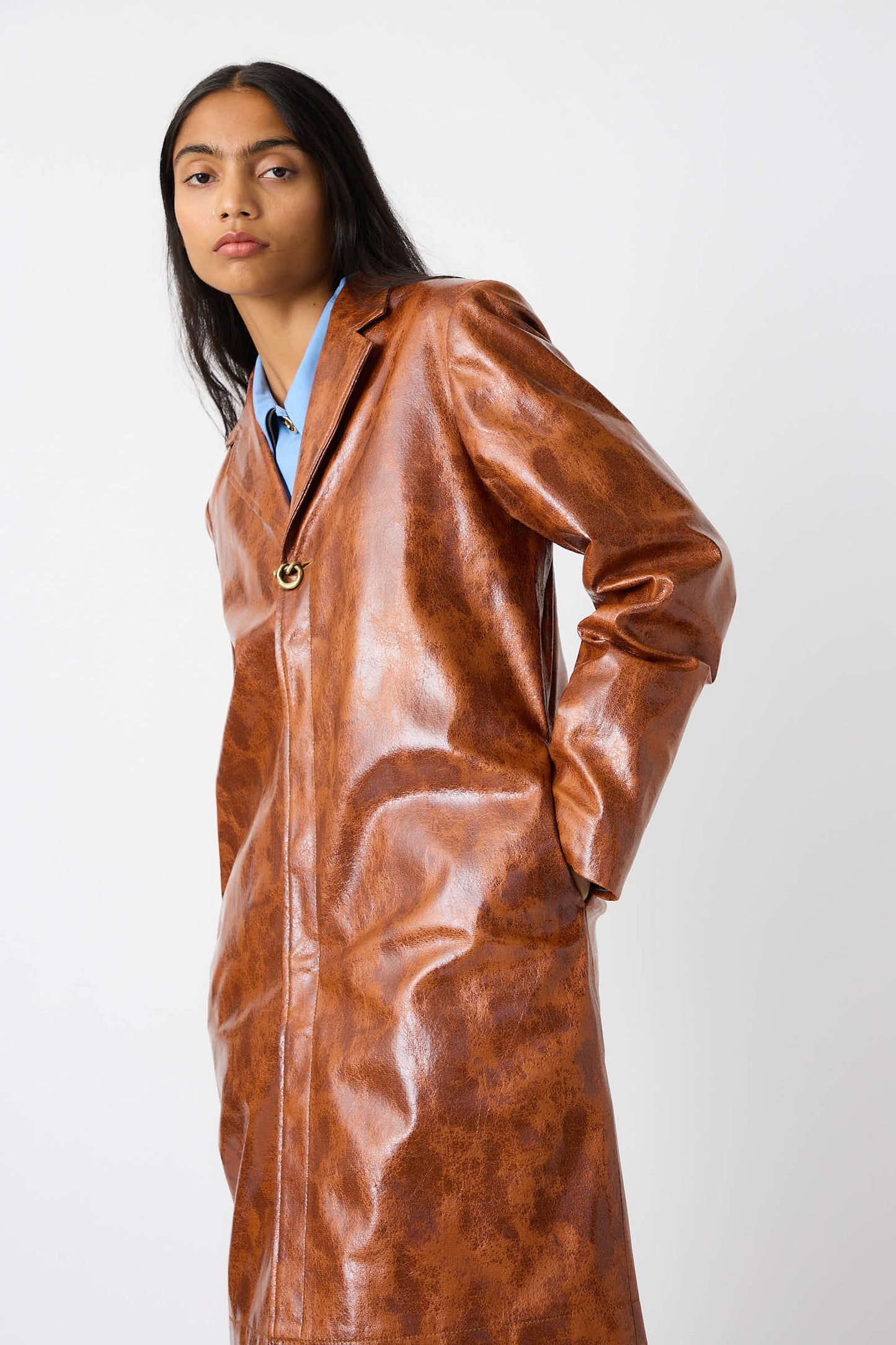 Person wearing the Faux Leather Samantha Jacket in Brown by Rejina Pyo, featuring a notched collar and textured finish, hands in pockets, posing in front of a plain white background.