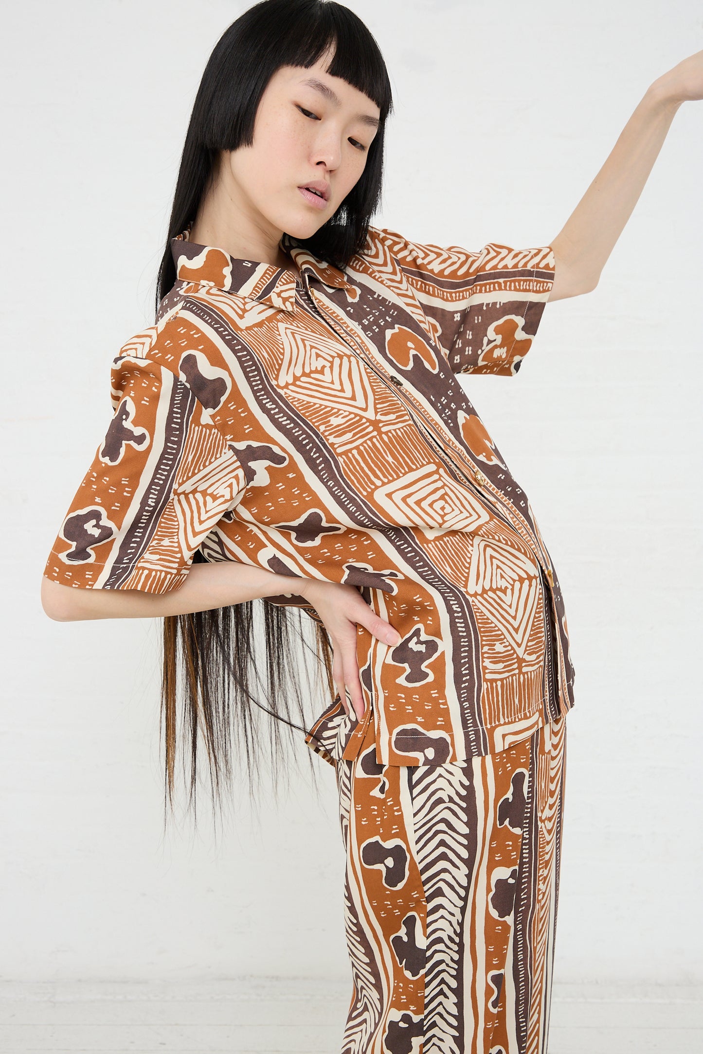A woman posing in a Rejina Pyo Marty Shirt in Print Brown outfit with her arm extended.