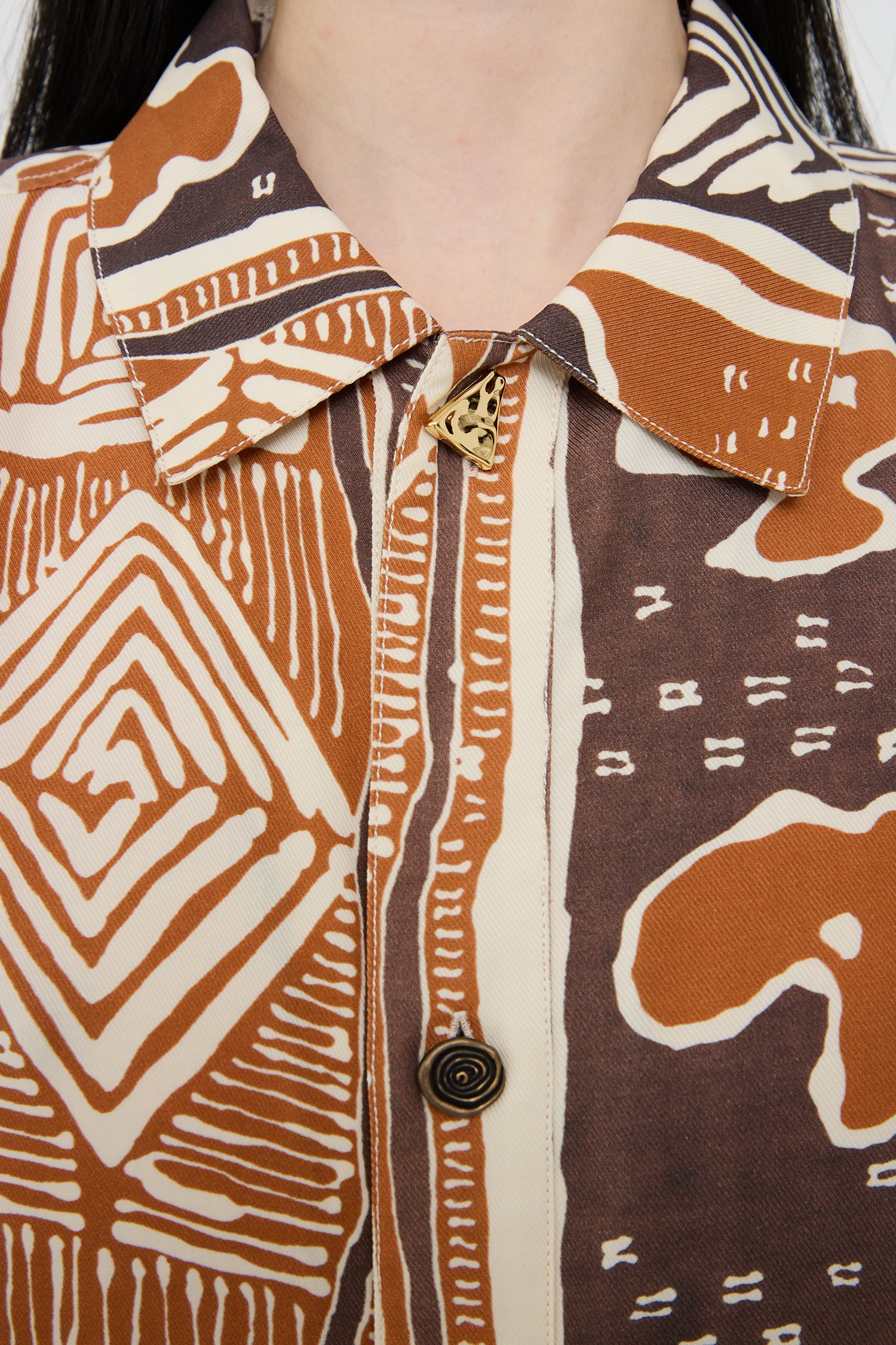 Close-up of a person wearing a Rejina Pyo Marty Shirt in Print Brown with an earth-toned, vintage-inspired hand-painted print and a decorative brooch on the collar.
