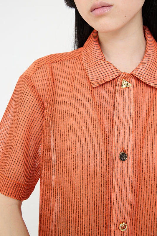 A close-up of a person wearing an Mesh Stripe Marty Shirt in Orange, designed by Rejina Pyo.
