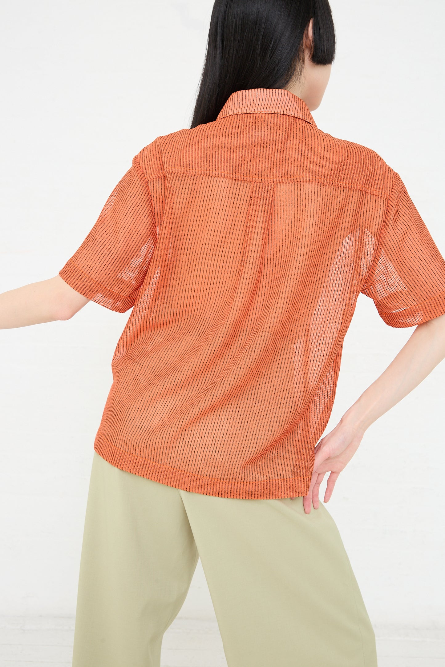 A woman seen from behind wearing a Rejina Pyo Mesh Stripe Marty Shirt in Orange and khaki pants.
