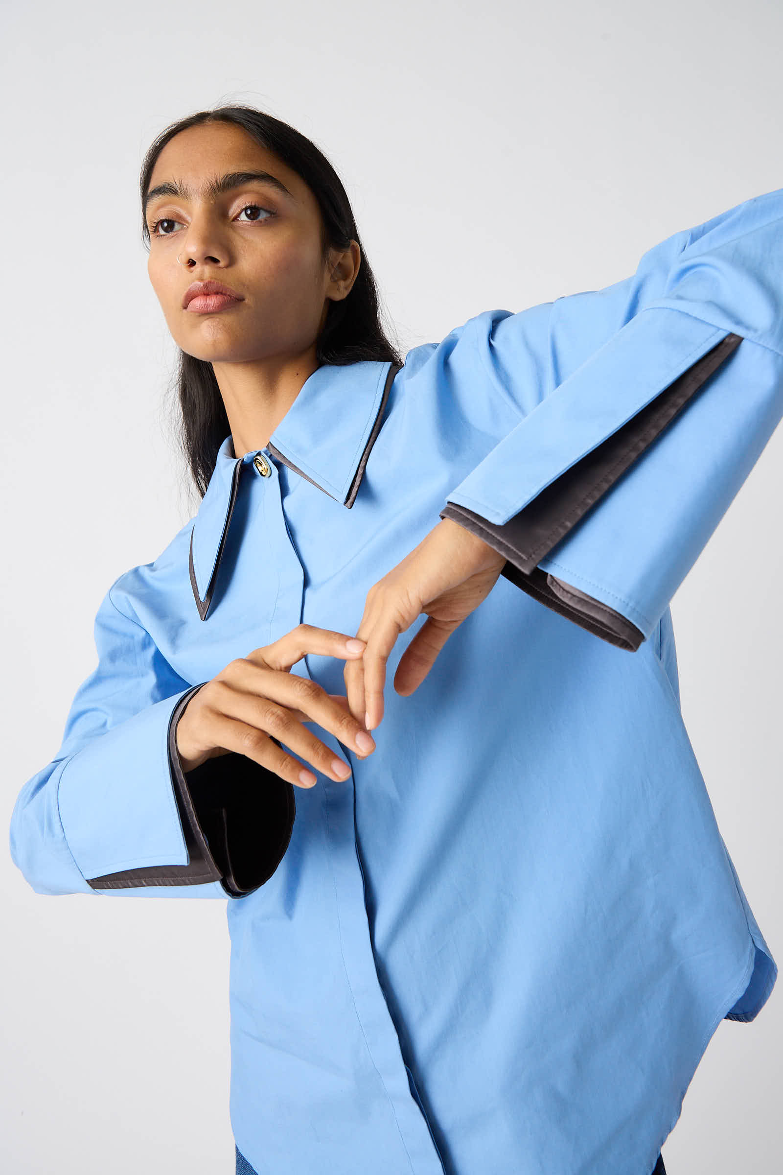 A person poses in an Organic Cotton Parker Shirt in Blue by Rejina Pyo, featuring a relaxed fit, long sleeves with wide cuffs, and a large collar against a plain background.
