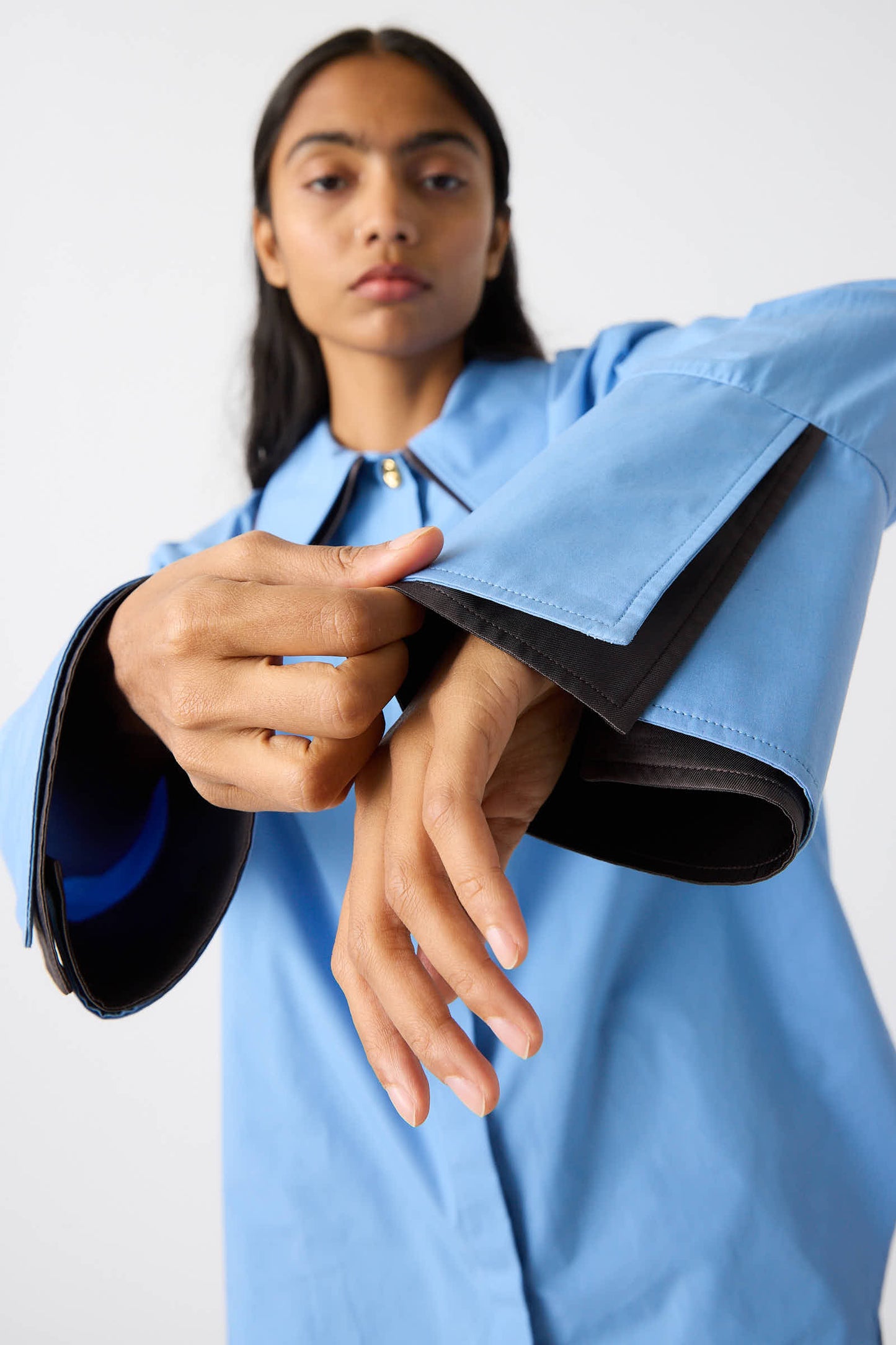 A person wearing the Rejina Pyo Organic Cotton Parker Shirt in Blue showcases the unique design, featuring oversized, flared sleeves with black lining and a front zipper closure. Made from organic cotton for added comfort.