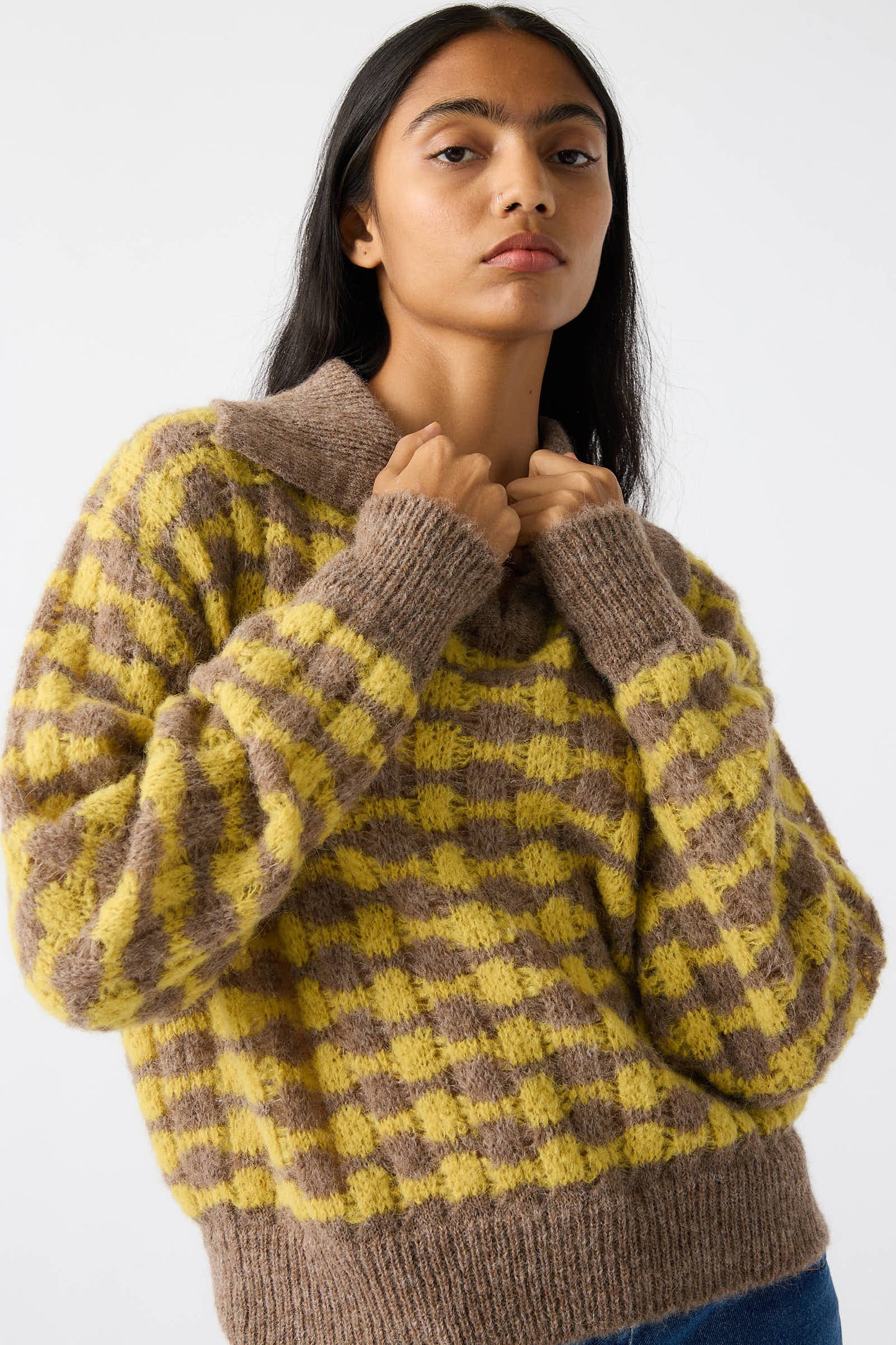 A person with long dark hair is wearing the Rae Sweater in Yellow from Rejina Pyo, while holding the sweater's collar.