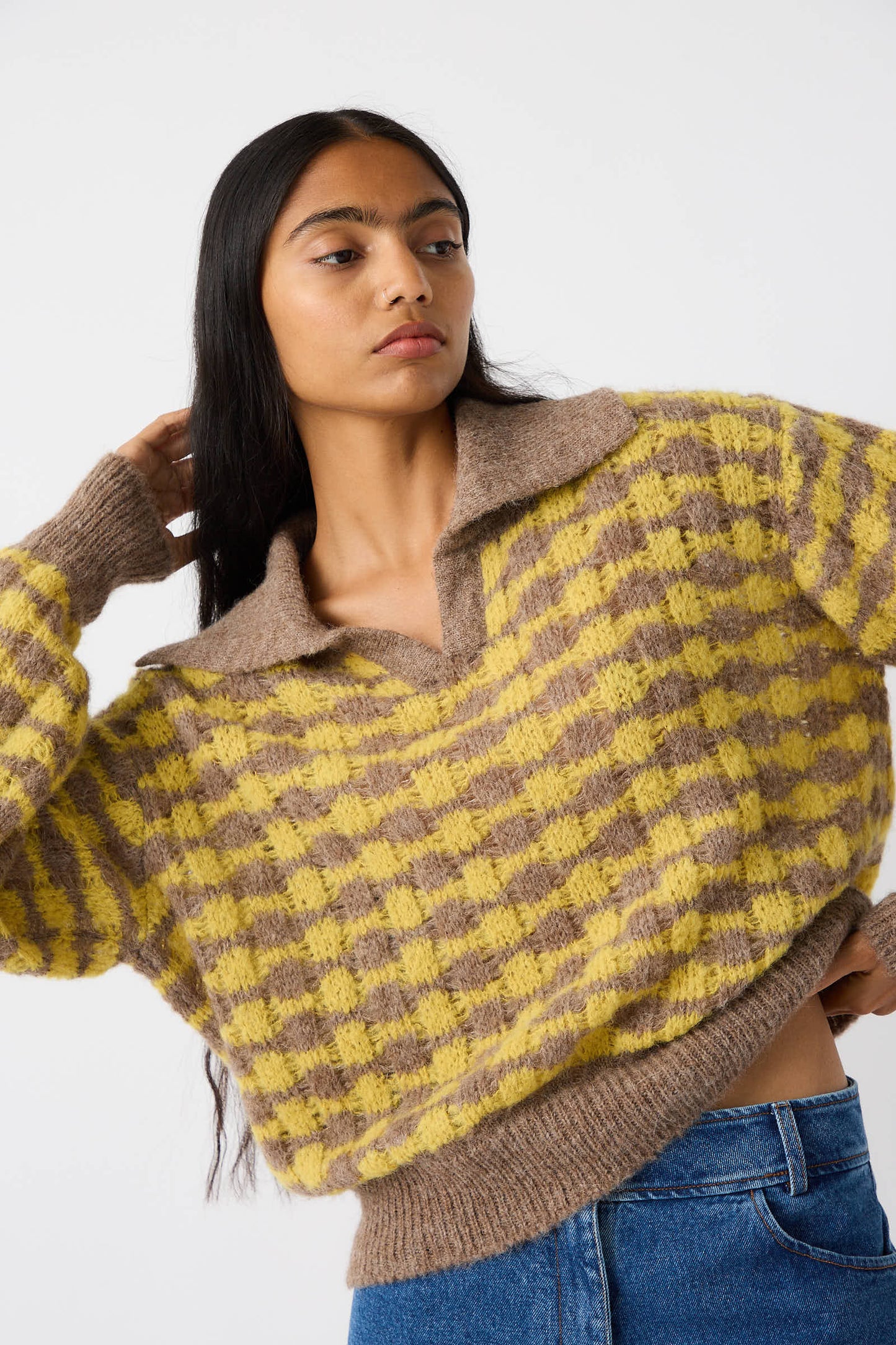 A person with long dark hair wears the Rae Sweater in Yellow, an alpaca blend knit by Rejina Pyo, with a hand behind their head and is dressed in blue jeans.