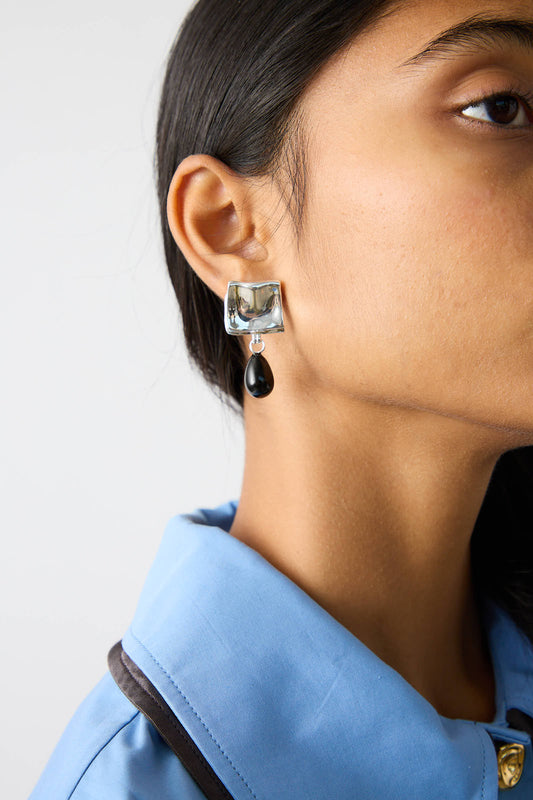 Close-up of a person wearing a blue collared shirt and Rejina Pyo's Silver Plated Folded Drop earrings with Black Onyx.