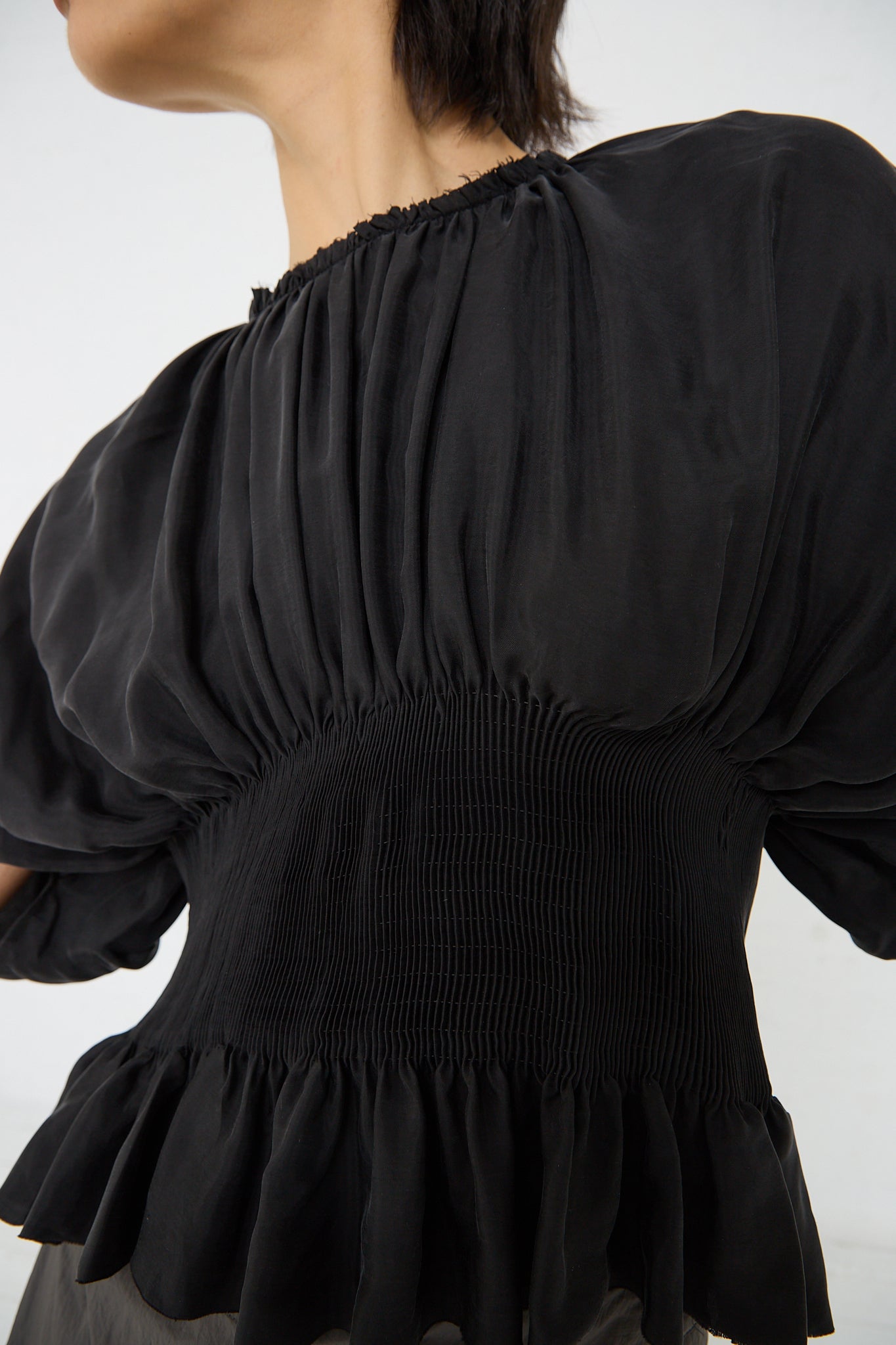 A woman wearing a Renata Brenha Cupro Sanfona Top in Washed Black with ruffles made from recycled cupro fabric.