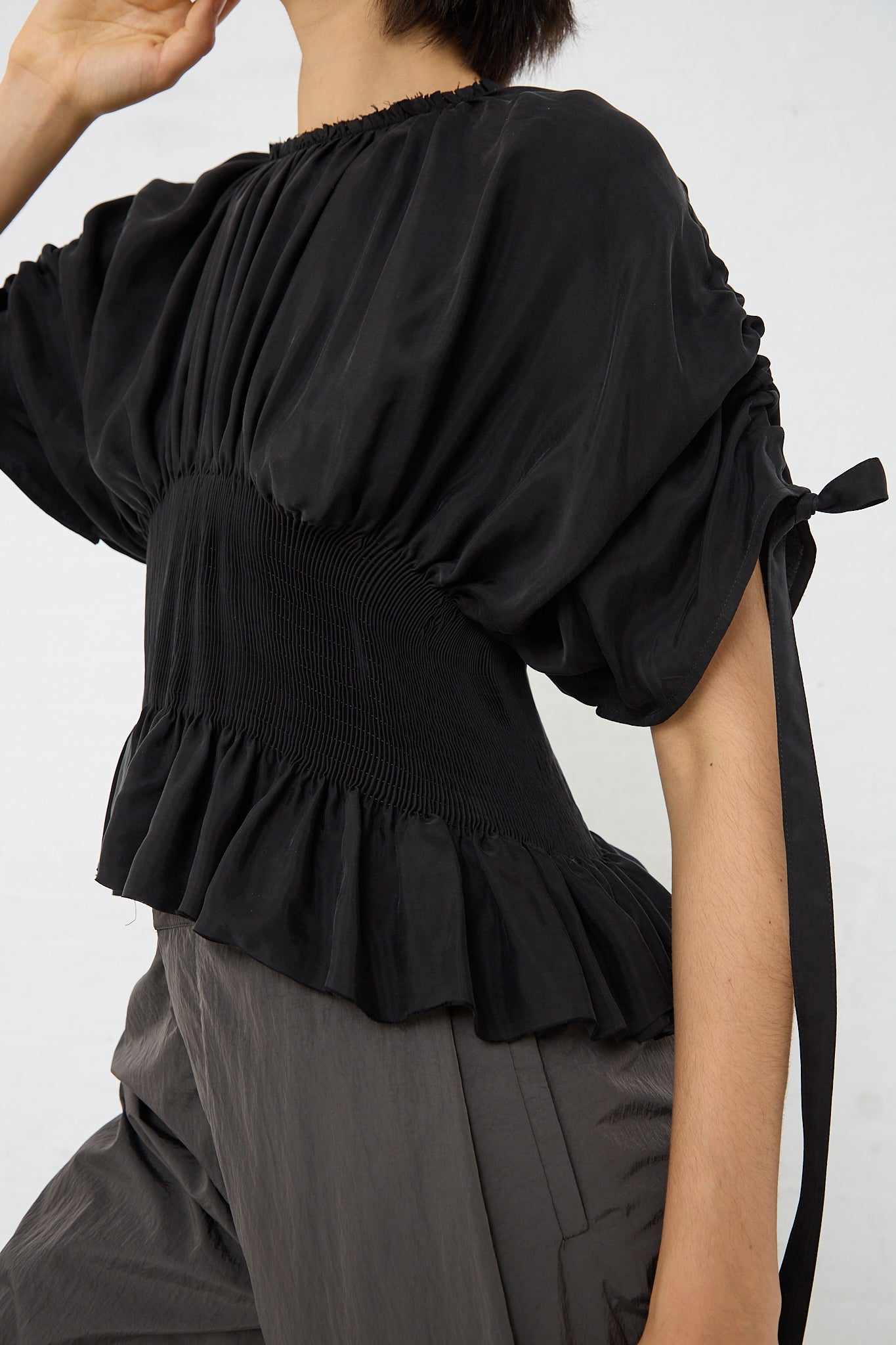 A woman wearing a Cupro Sanfona Top in Washed Black made by Renata Brenha with ruffles made from recycled cupro. Side view.