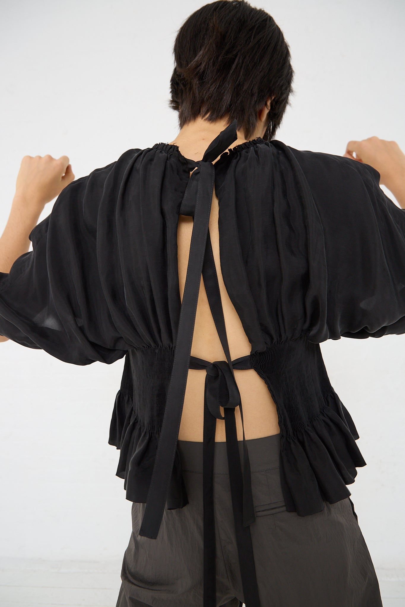 The back of a woman wearing a Renata Brenha Cupro Sanfona Top in Washed Black adorned with two bows made with recycled cupro fabric.