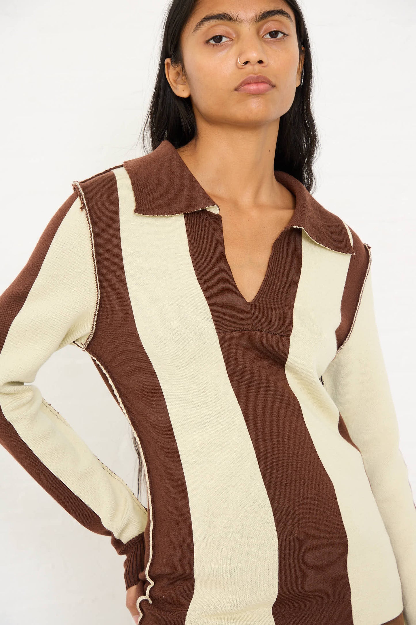 A person with long dark hair wearing the Renata Brenha Mané Polo Knit in Cream and Brown, inspired by 70s football jerseys, standing against a plain white background.