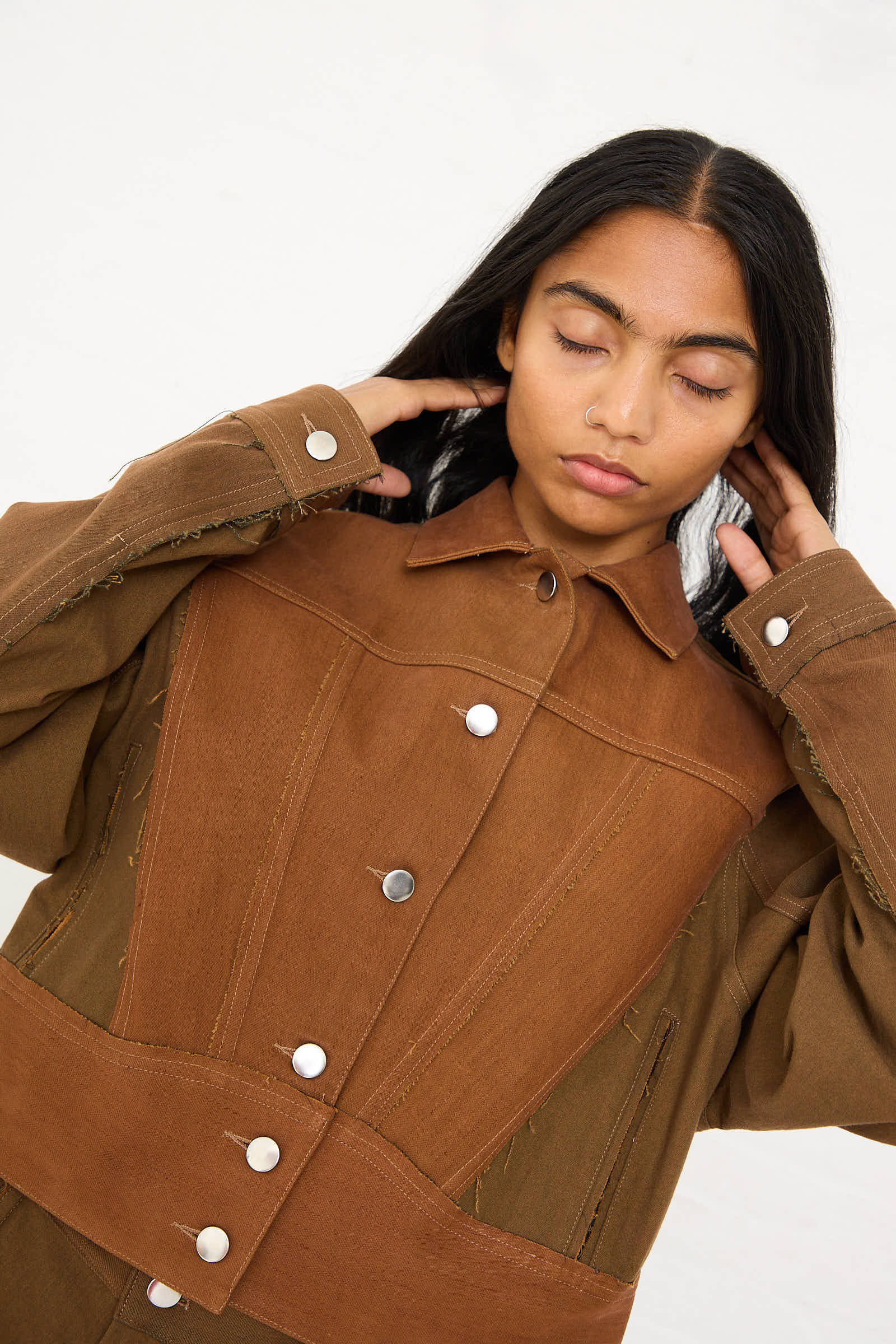 A person wearing a relaxed fit, Upcycled Denim Cangaço Jacket in Brown by Renata Brenha touches their neck with closed eyes.