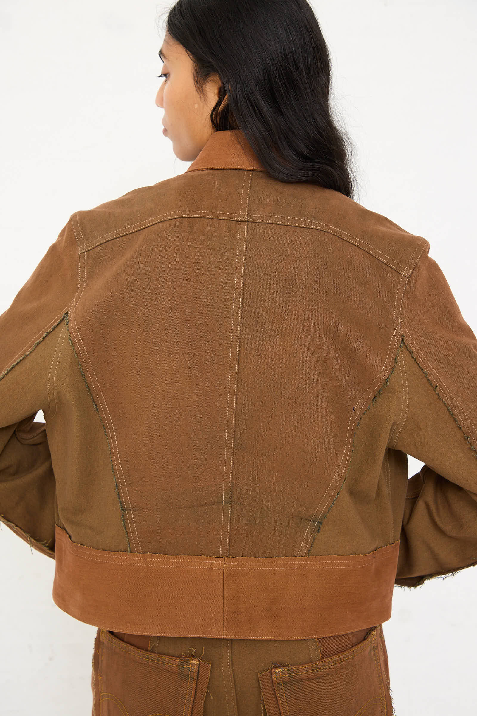 A person wearing the Renata Brenha Upcycled Denim Cangaço Jacket in Brown, featuring a fitted waist and loose sleeves with visible stitching details, is shown from the back, facing slightly to the right.