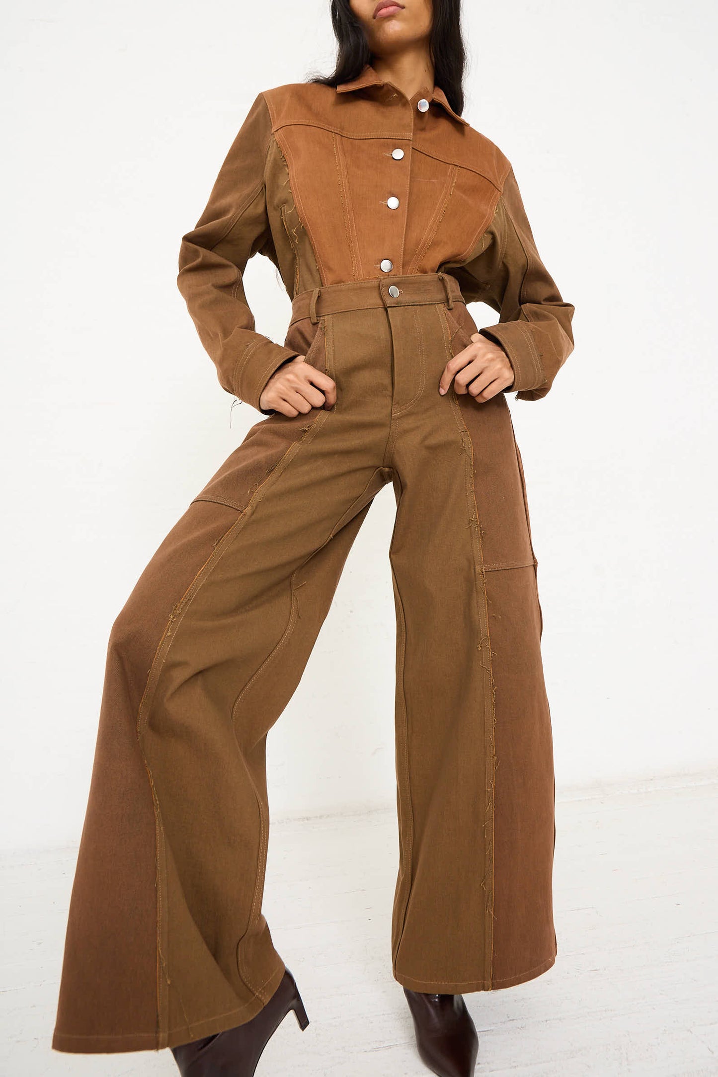 A person modeling the Renata Brenha Upcycled Denim Cangaço Trouser in Brown, featuring wide-leg pants with a button-up front and long sleeves. The relaxed fit outfit is contrasted with darker and lighter brown panels.