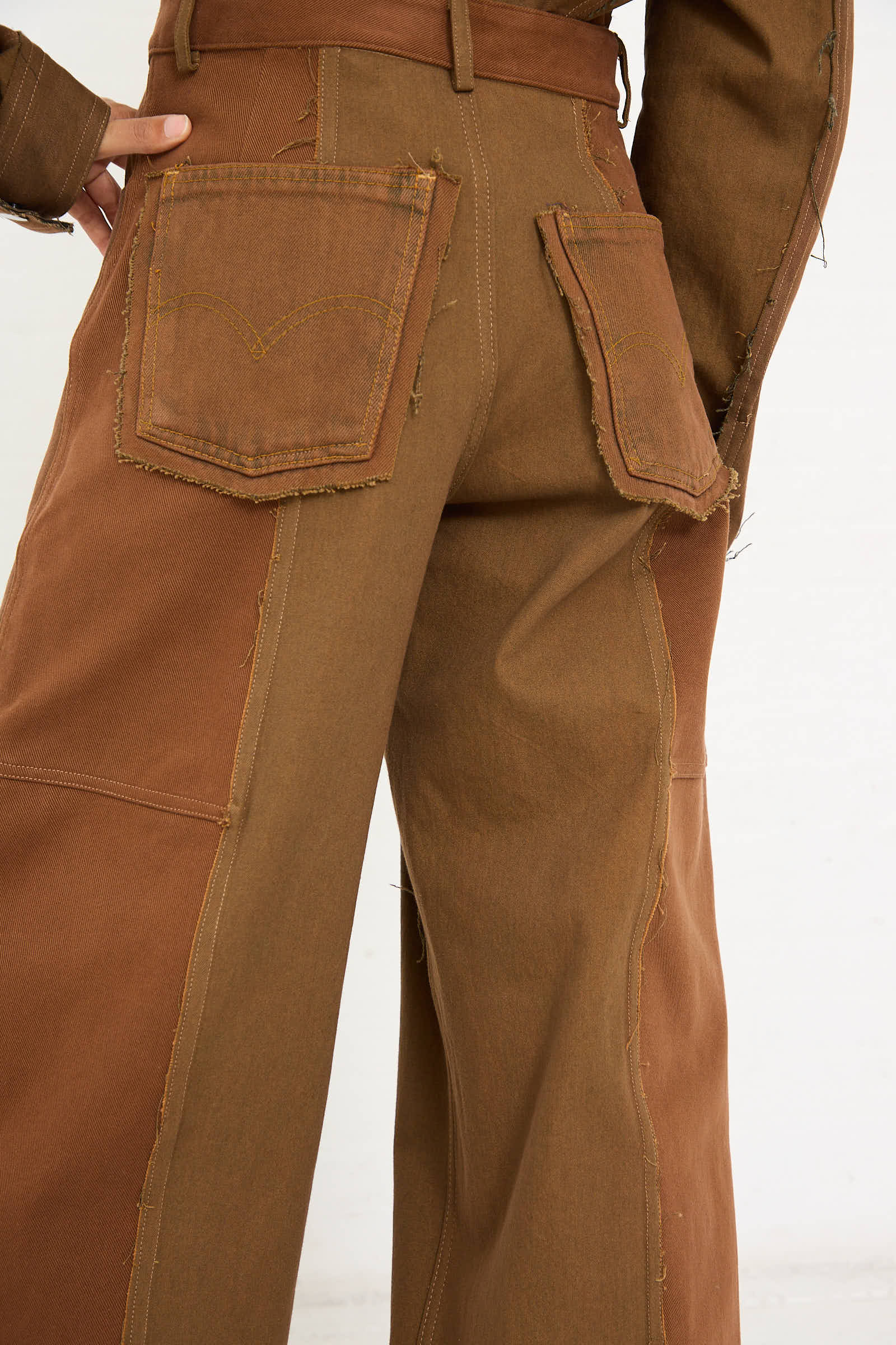 Close-up of the back of a person wearing the Upcycled Denim Cangaço Trouser in Brown by Renata Brenha. The relaxed fit, two-tone brown patchwork pants are oversized and feature visible stitching and frayed edges around the pockets and seams, made from upcycled denim.