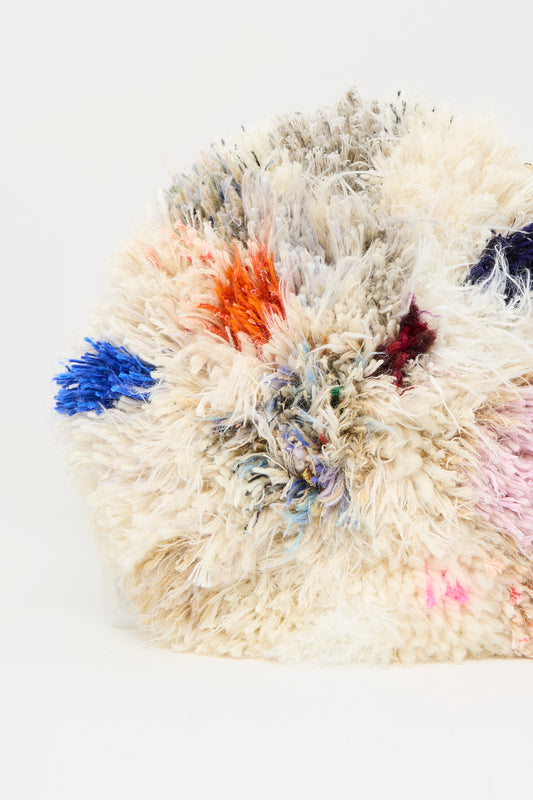 A close-up of the Handmade Cushion in Multi IX by Renilde De Peuter, featuring fluffy multicolored blue, orange, pink, and purple fibers crafted with the smyrna stitch technique against a white background.