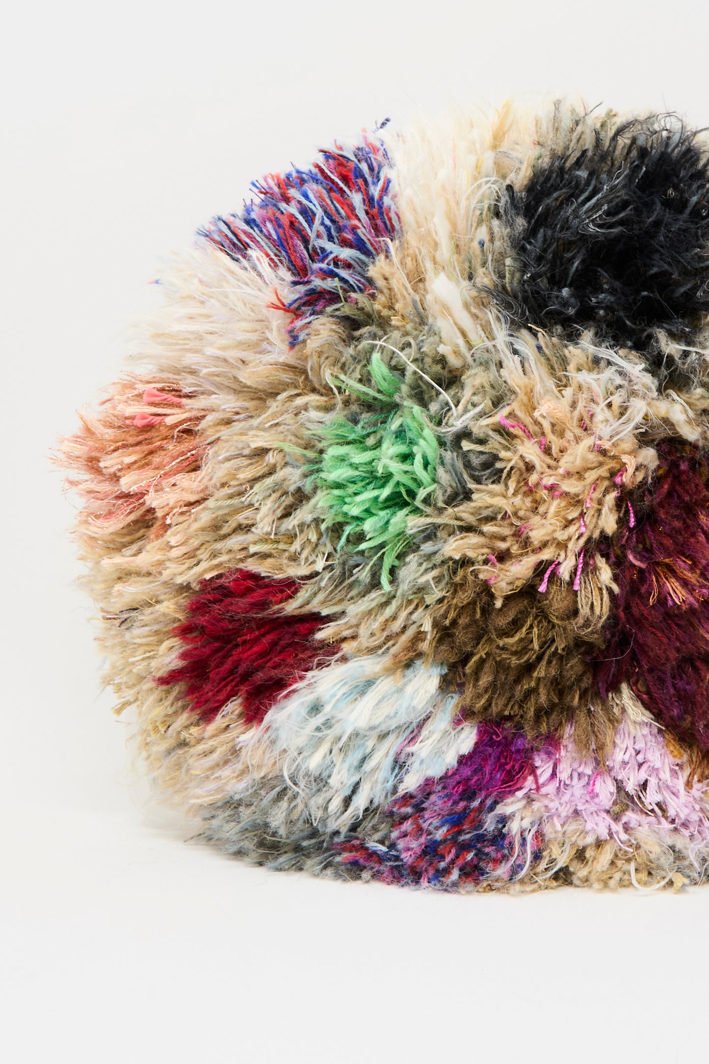 A close-up of the Handmade Cushion in Multi V by Renilde De Peuter, a shaggy, round seat cushion made from recycled yarns with vibrant patches, showcased against a plain white background.