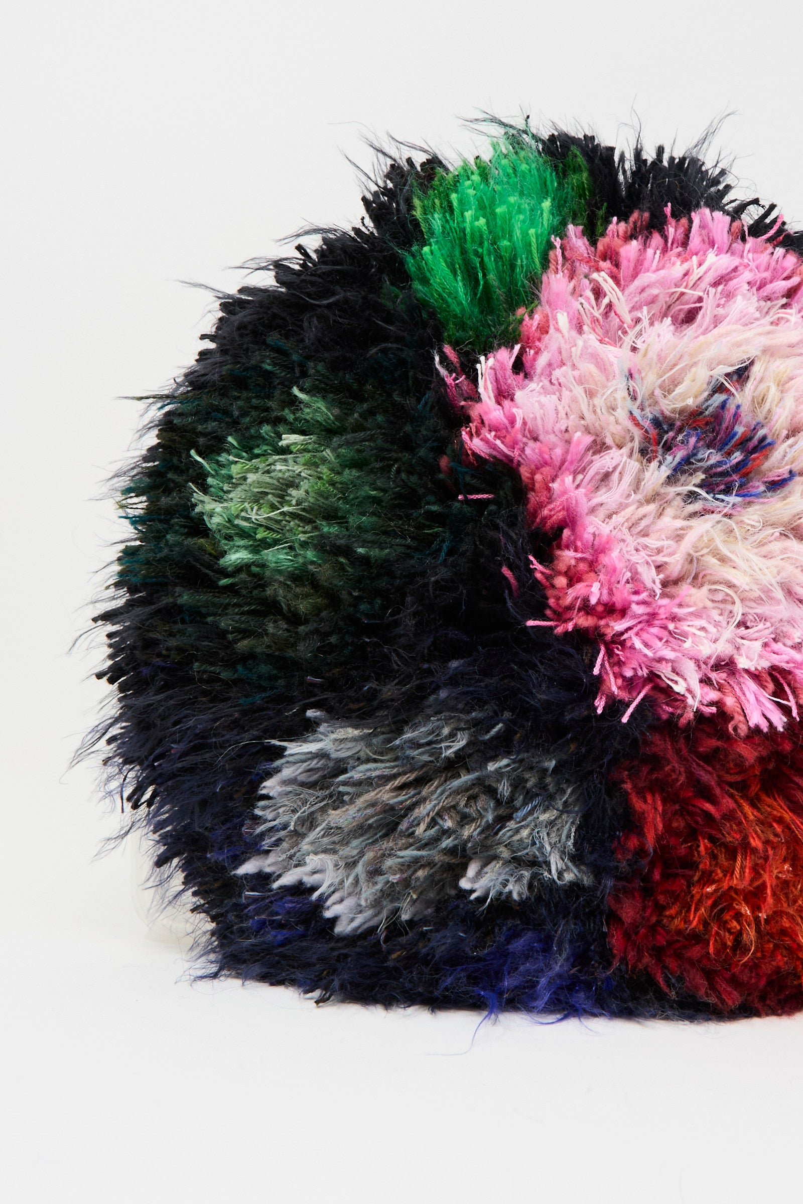 A close-up of the Handmade Cushion in Multi XIV by Renilde De Peuter, a circular, multicolored seat cushion made with colorful fabrics using the smyrna stitch, displayed against a plain white background.