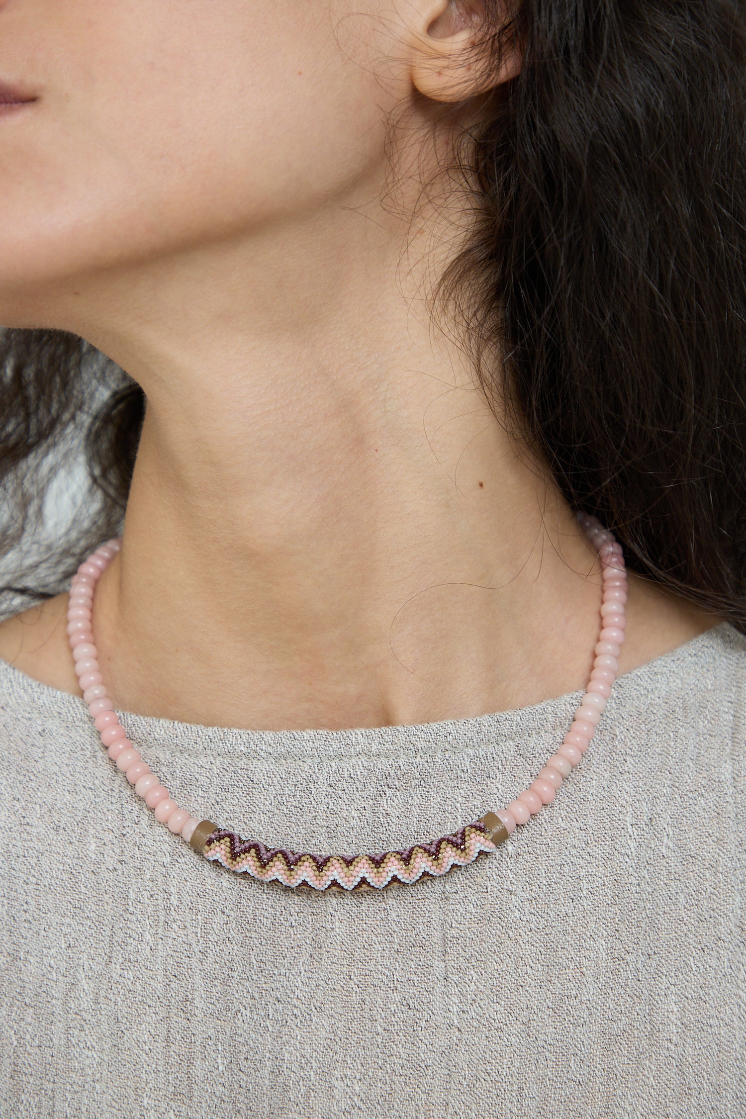 Close-up of a woman wearing a Robin Mollicone Beaded Bar Necklace in Pink Opal with a zigzag pattern detail.