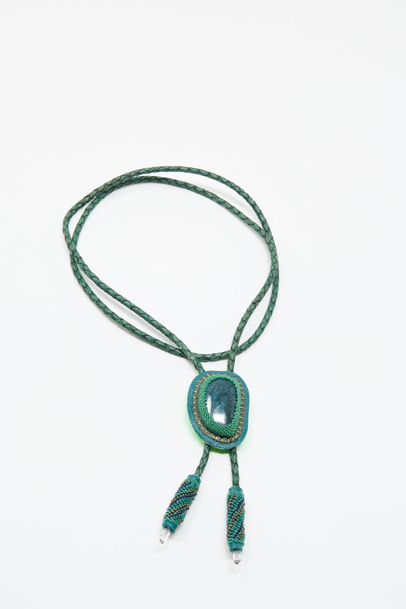 The Robin Mollicone Bolo Necklace in Apatite and Quartz features a green braided cord, an oval apatite pendant, and two beaded tassels, all displayed on a white background.