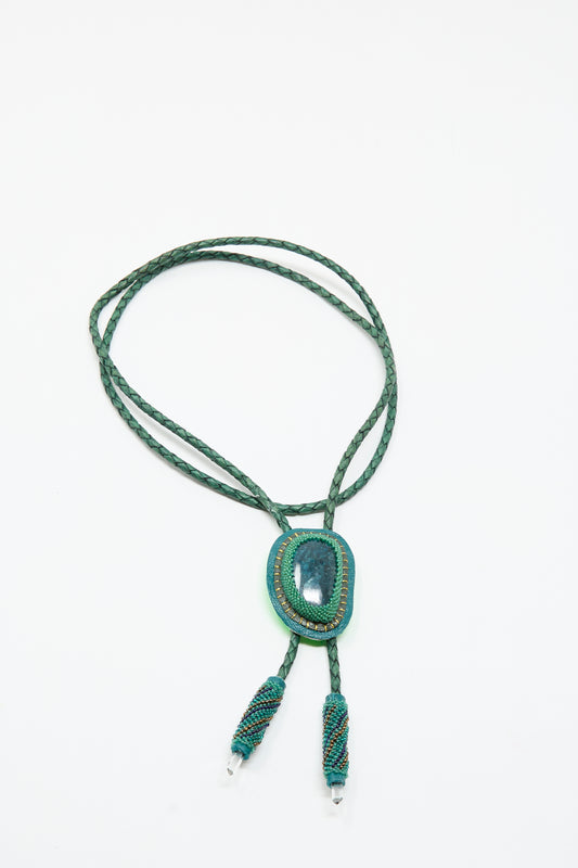 The Robin Mollicone Bolo Necklace in Apatite and Quartz features a green braided cord, an oval apatite pendant, and two beaded tassels, all displayed on a white background.
