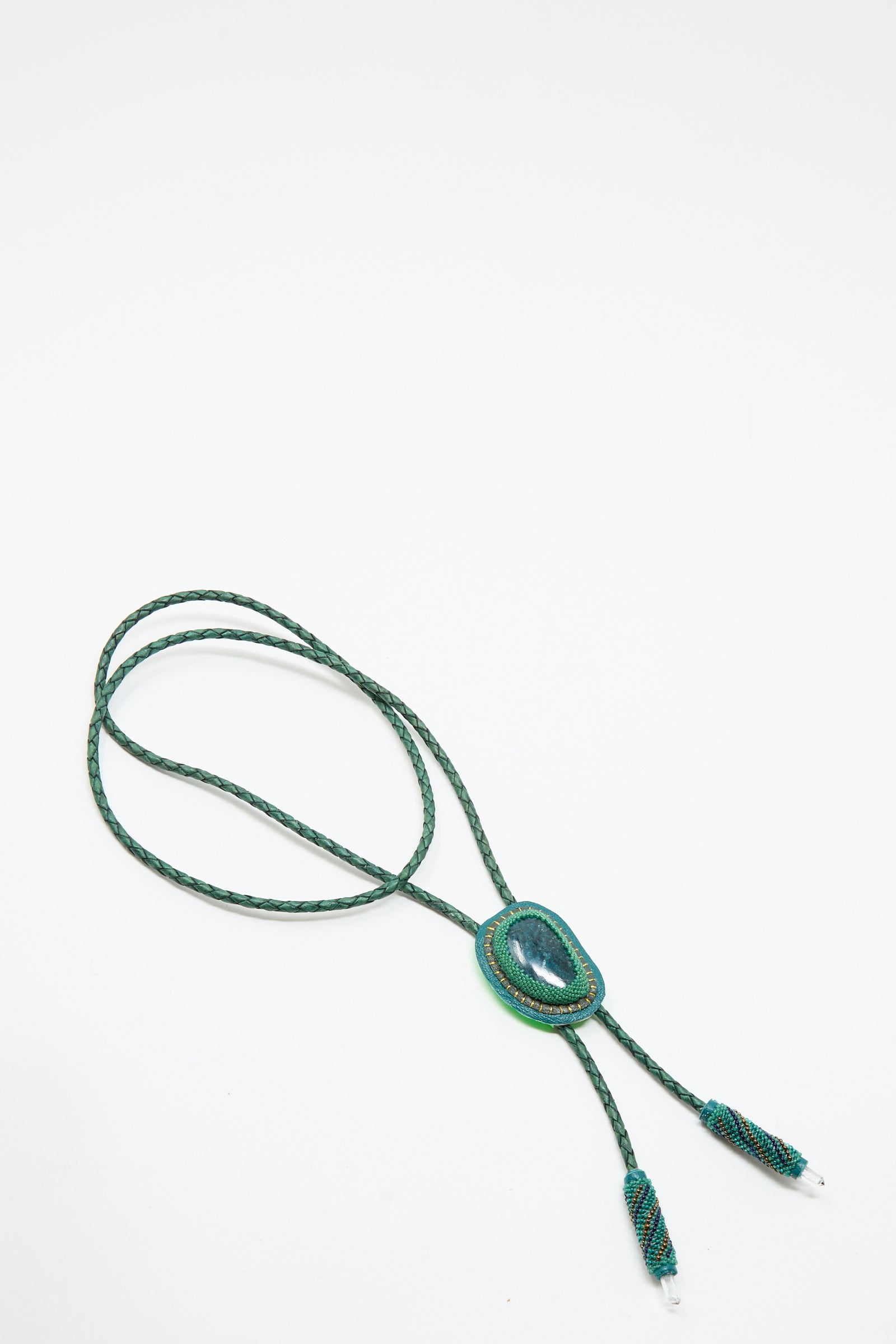 The Robin Mollicone Bolo Necklace in Apatite and Quartz features a green braided cord, a central oval quartz stone, and decorative metal tips, all shown against a plain white background.