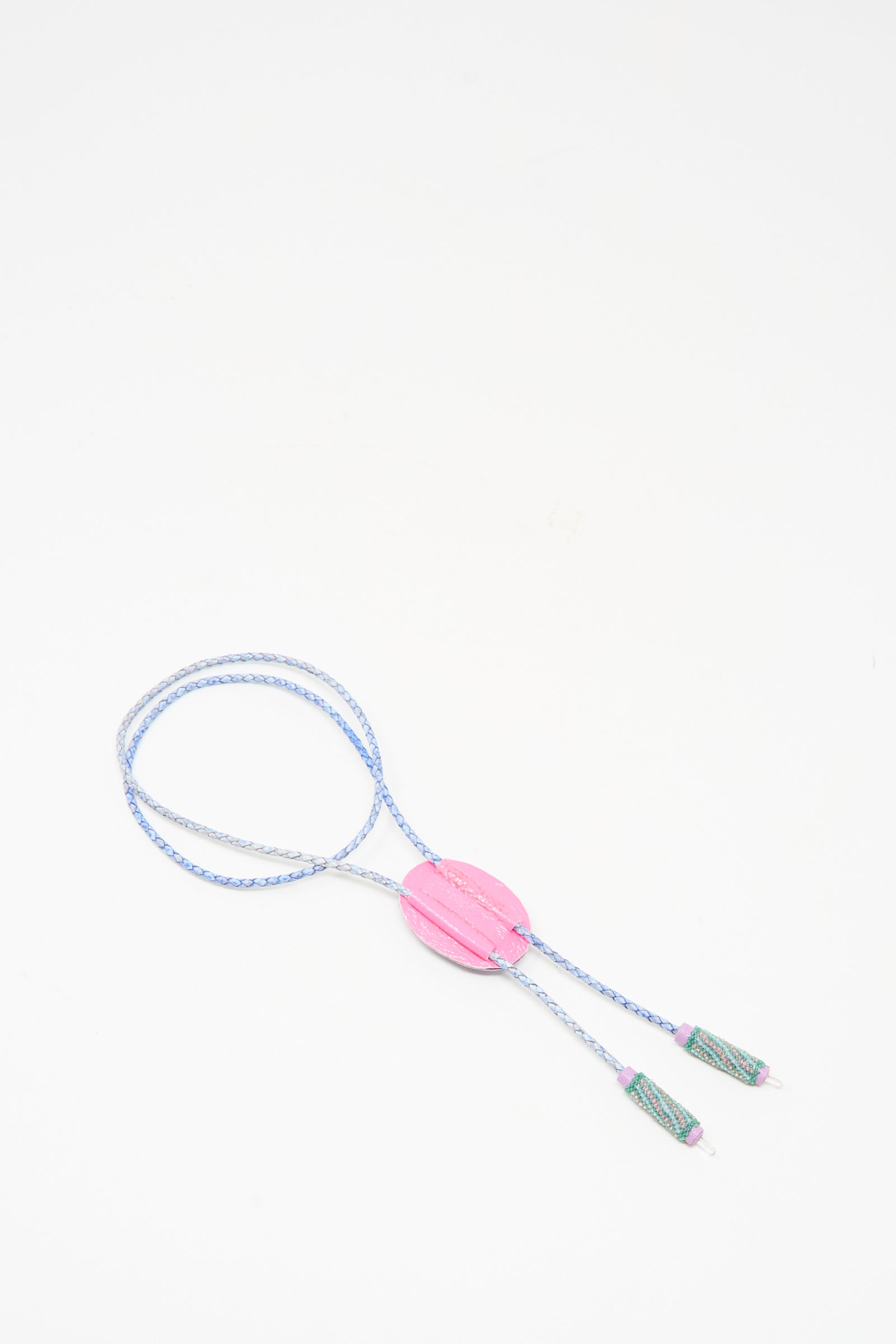 The Robin Mollicone Bolo Necklace in Kunzite and Quartz is a handmade blue and white braided cord necklace with a large pink oval bead center and two green tassels, shown on a white background.
