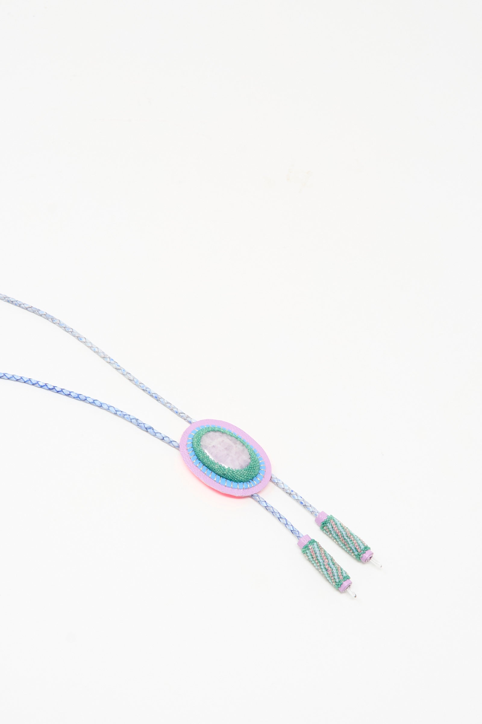 The Bolo Necklace in Kunzite and Quartz by Robin Mollicone features a beaded oval pendant with a central stone on a braided blue cord with tassel ends, handcrafted in NYC and photographed on a white background.