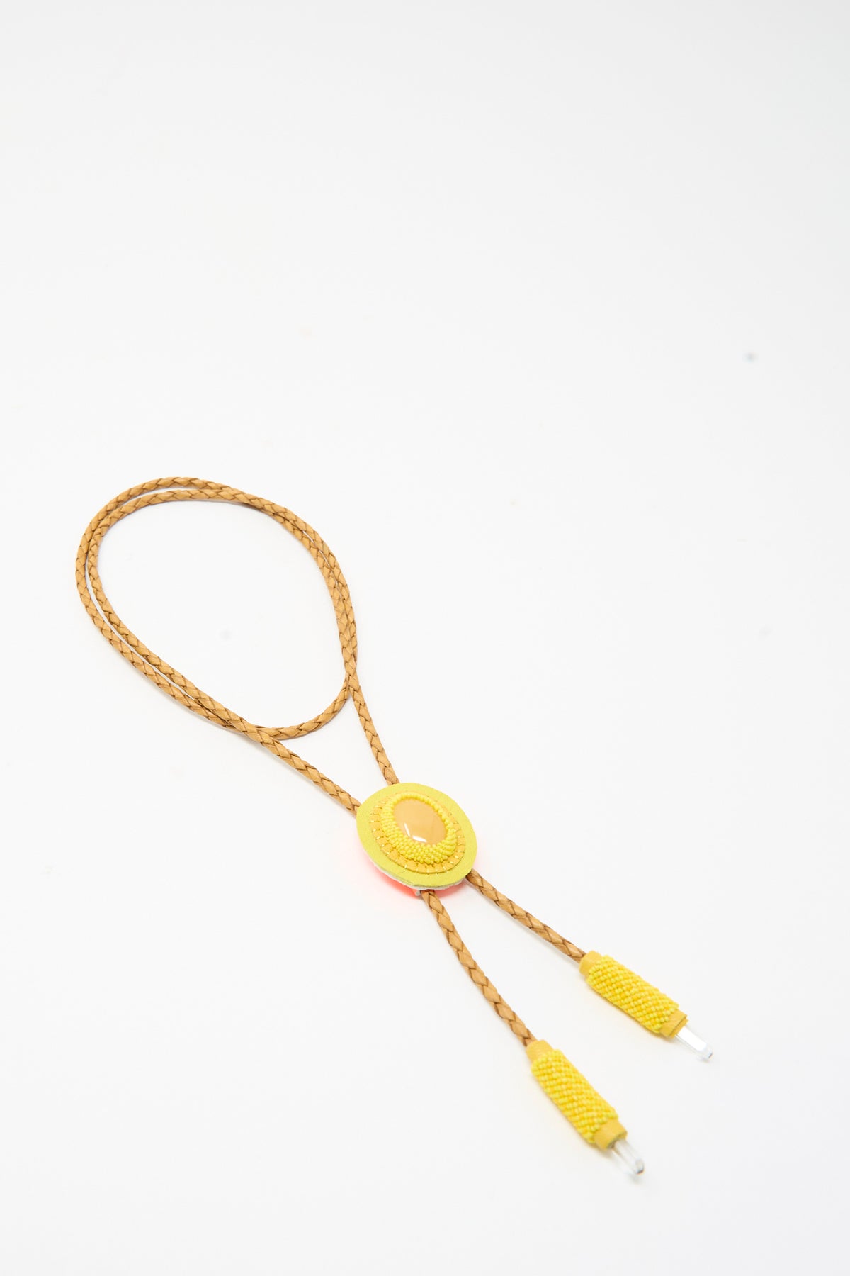 A Robin Mollicone Bolo Necklace in Yellow Calcite featuring an oval-shaped cabochon centerpiece on a braided tan cord with matching yellow cord ends.
